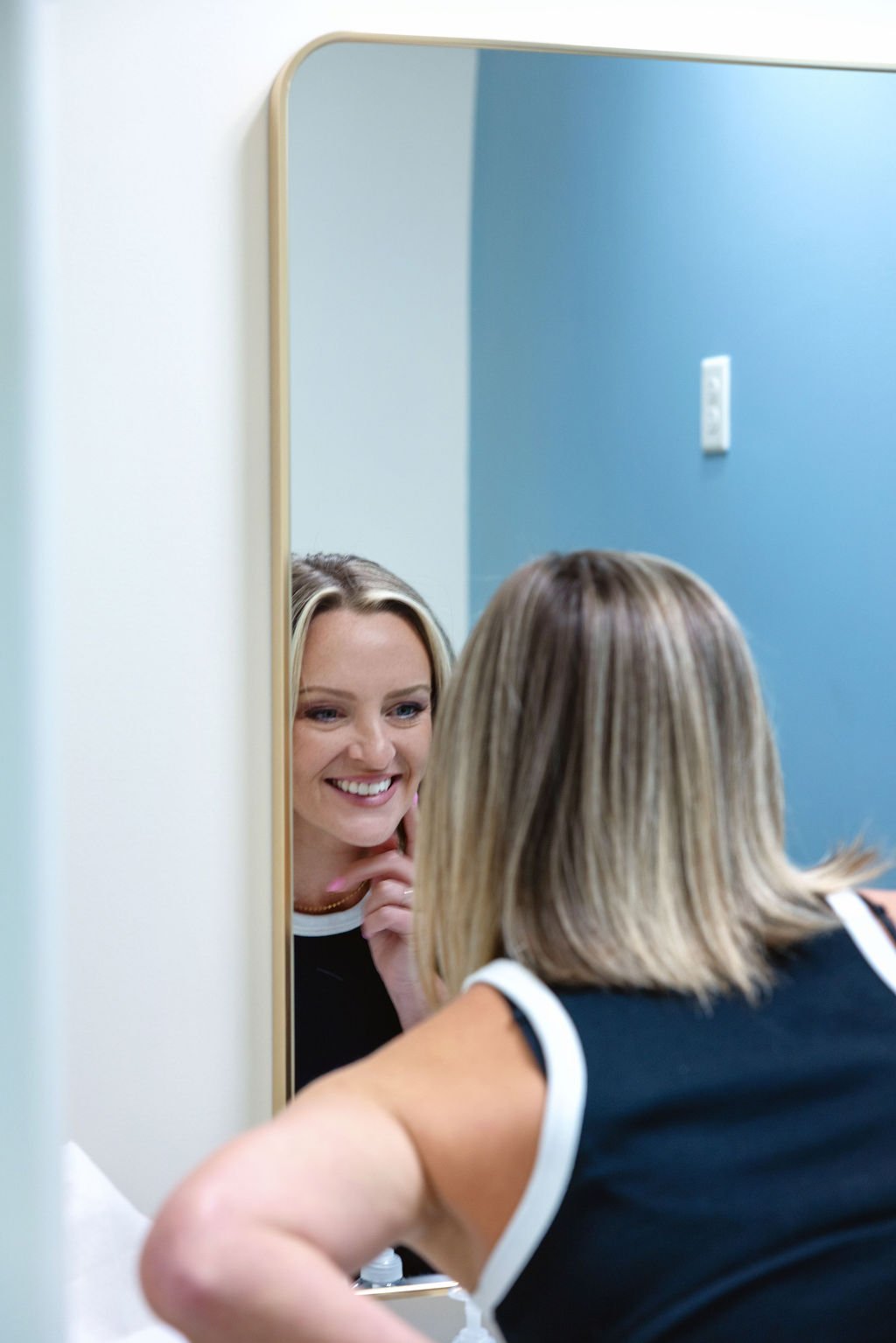 Adult woman smiling confidently at her reflection after orthodontic treatment at a Wichita area orthodontic office.
