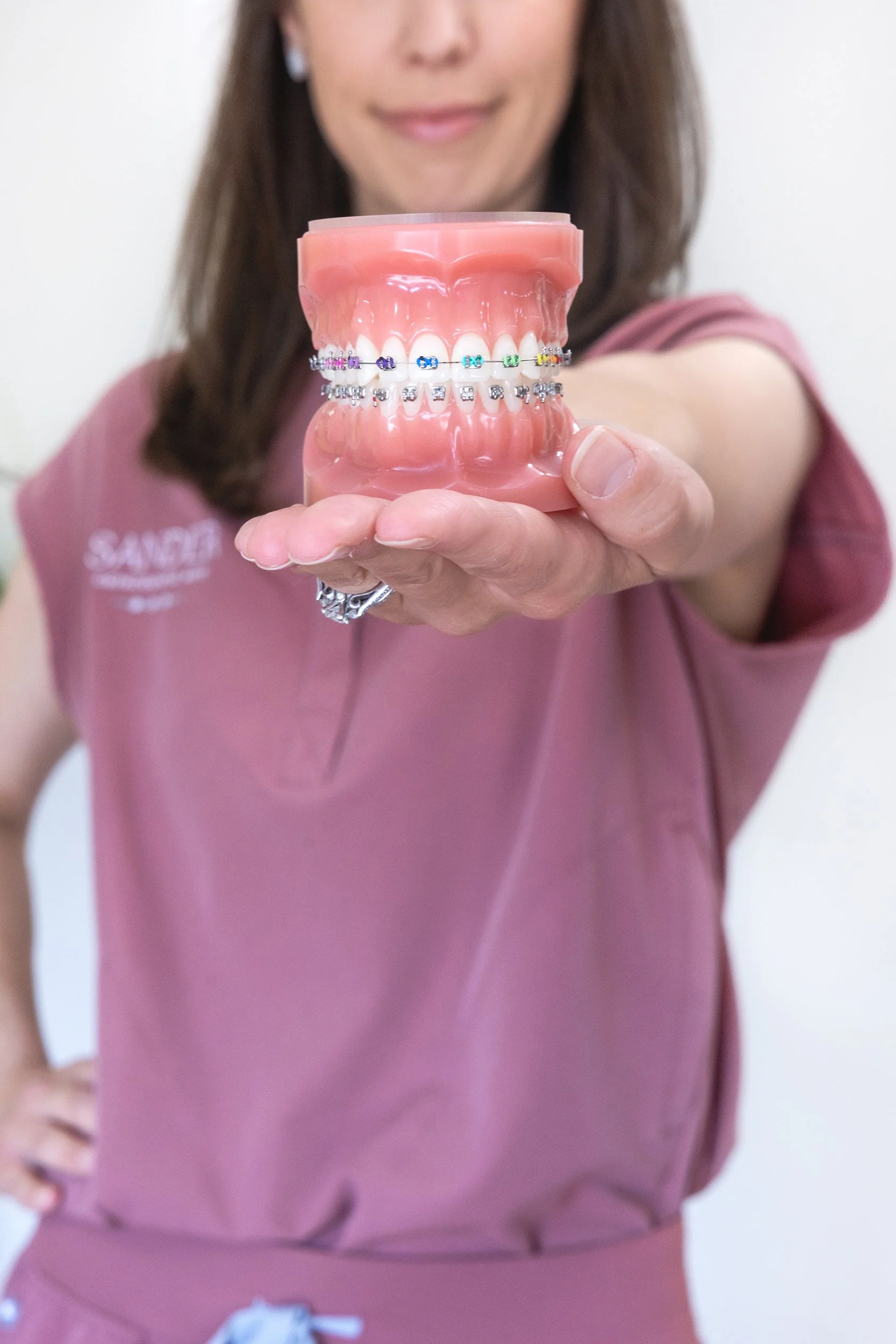Orthodontic team member holding a dental model with metal braces and colorful elastic ties.