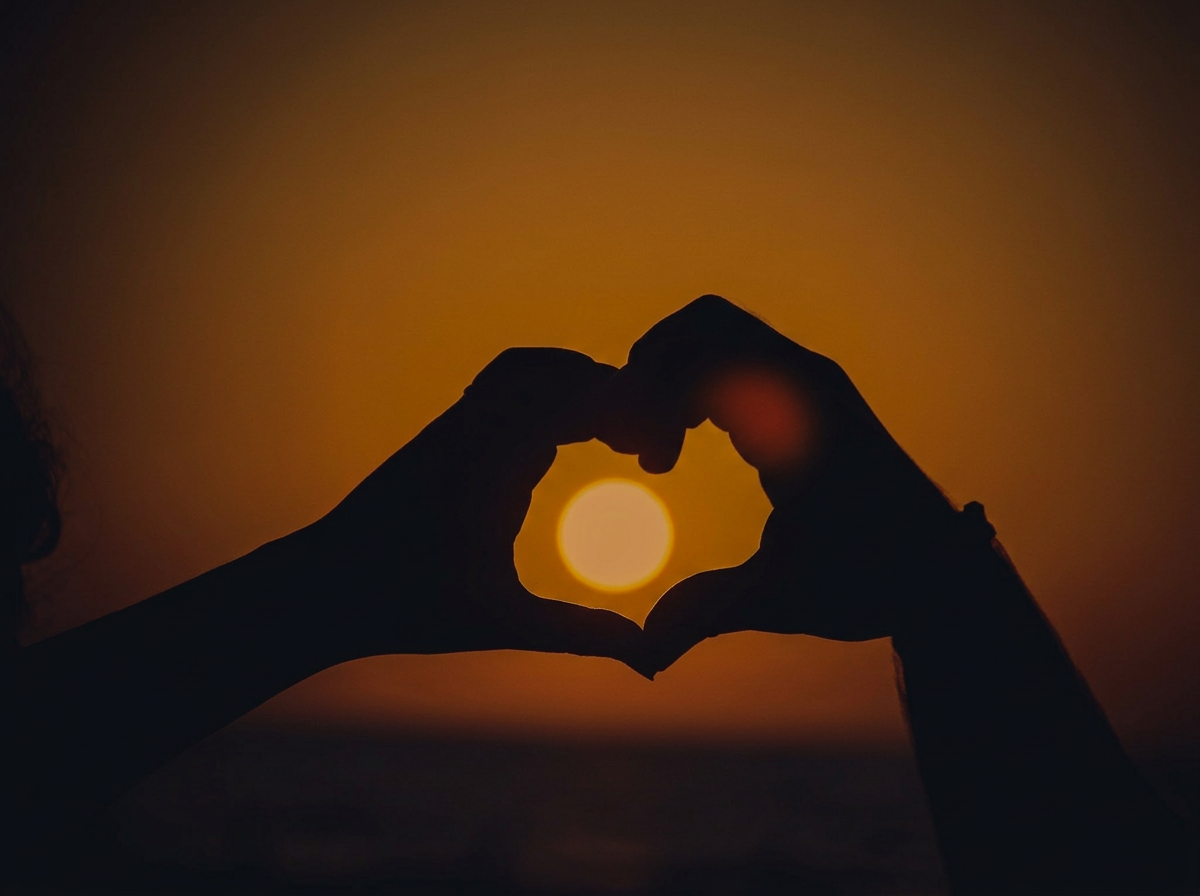 Image of two hands making a heart shape with the sun set behind  them