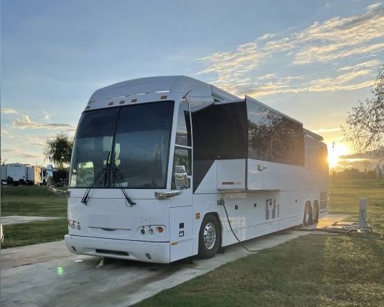 Luxury white RV parked on a concrete pad at sunset, with slide-out extended and cord connected to services.