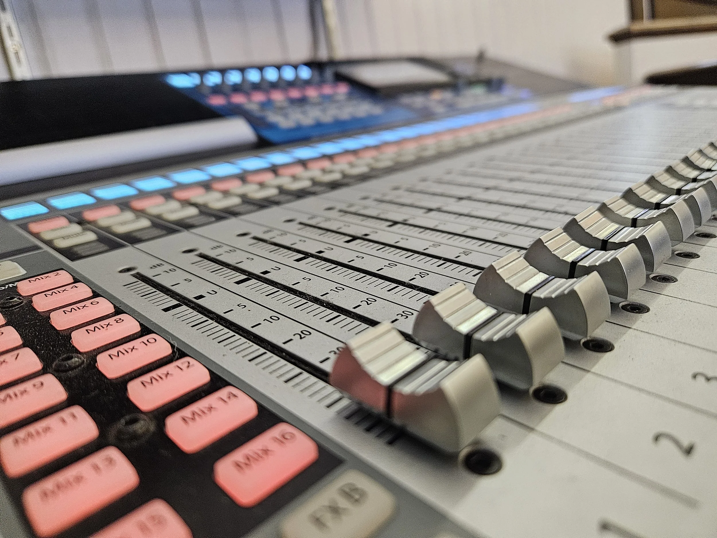Close-up of a professional audio mixing console with faders, knobs, and buttons.
