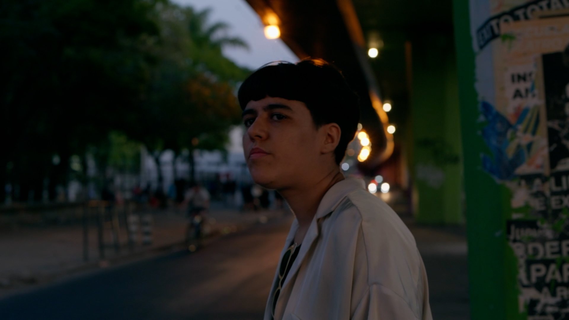 Moras de Ino Guridi. cabello corto, caminando en una calle iluminada con luces nocturnas bajo un puente.