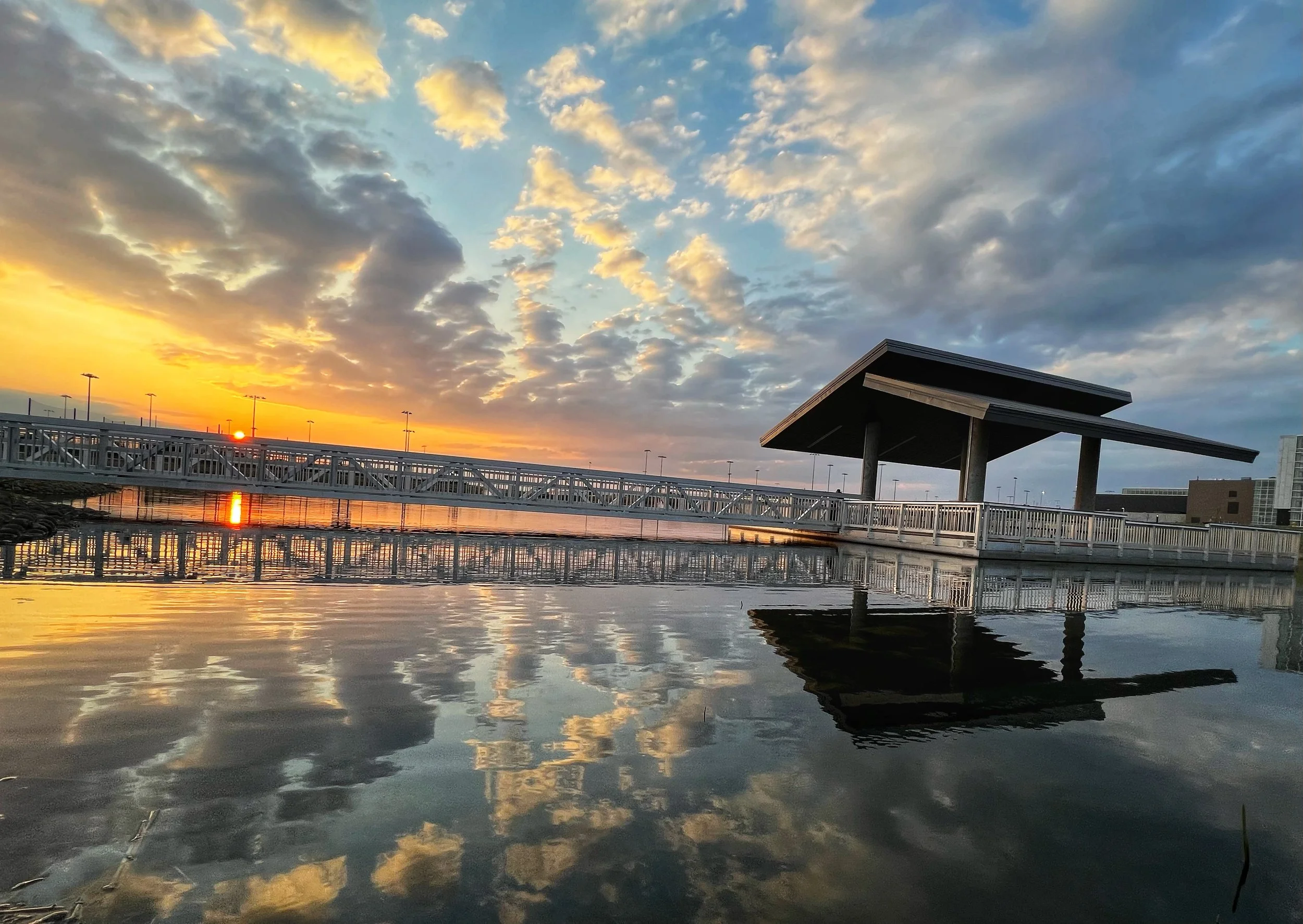 Sunset reflecting on water with a modern dock structure and dramatic clouds.