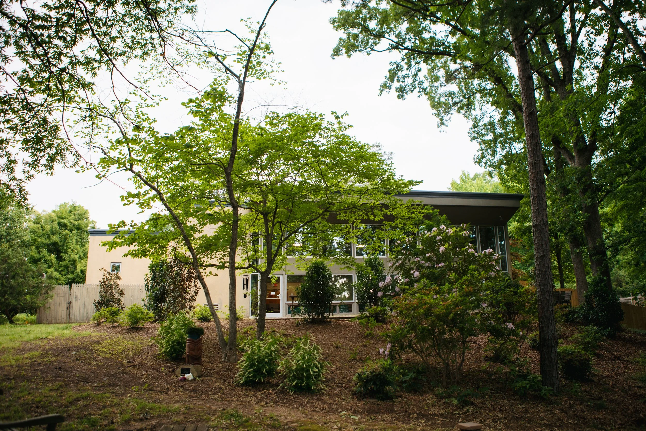 The long, one-level building of Piedmont Unitarian Universalist and its sanctuary's tall wall of windows are glimpsed through the woods behind the structure