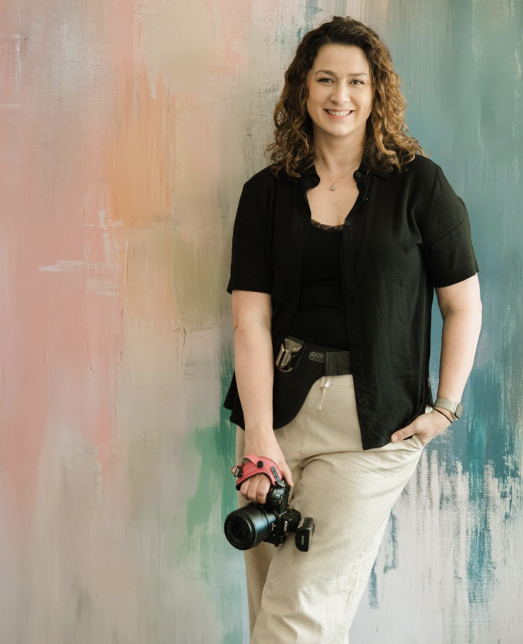 Jaimié, a professional photographer, smiles while holding a camera
