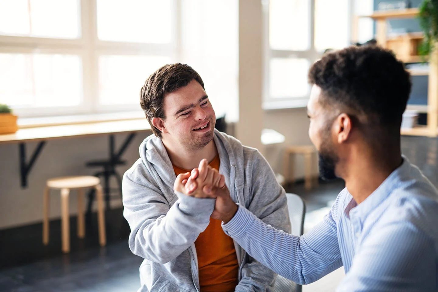 Two men smiling and shaking hands in a casual indoor setting.
