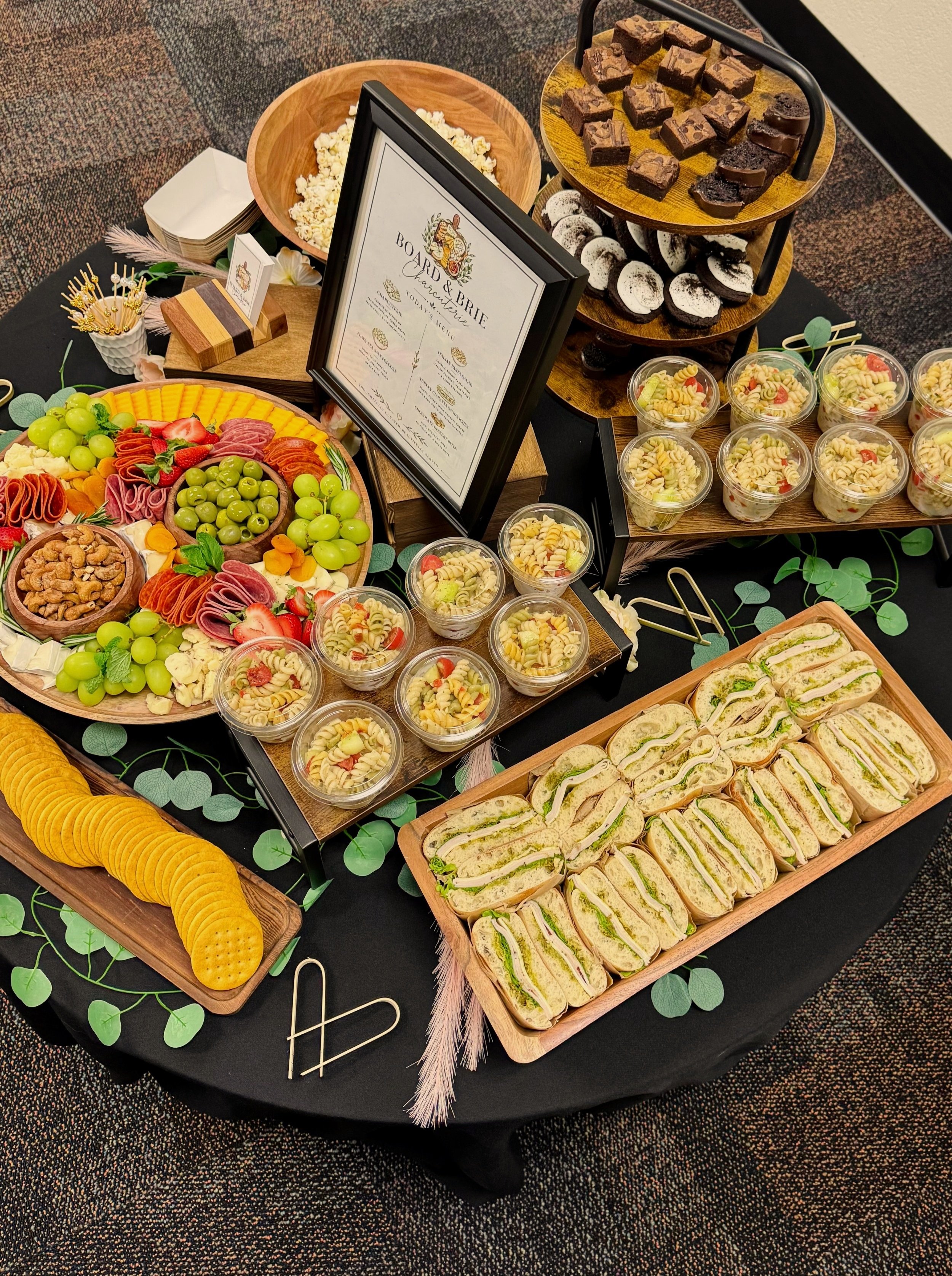 Assorted fruit, cheese, and meat displayed on black wooden trays on kitchen countertop for a buffet or snack setup.