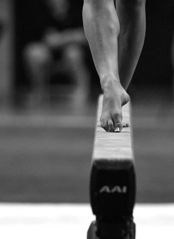 Close-up of a gymnast's bare feet balancing on a beam during a gymnastics routine.