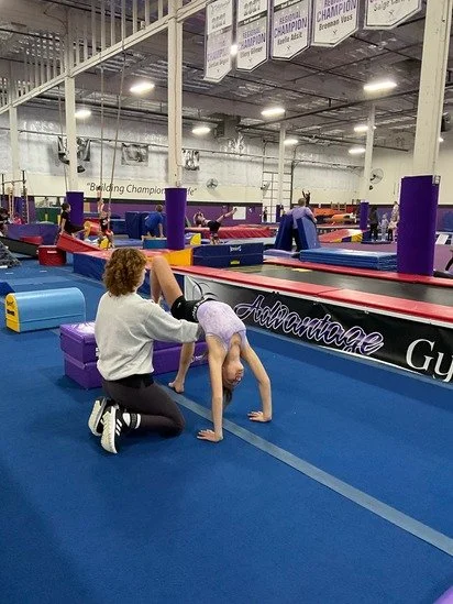 A gymnast practicing handstands in an indoor gym with coaching assistance.