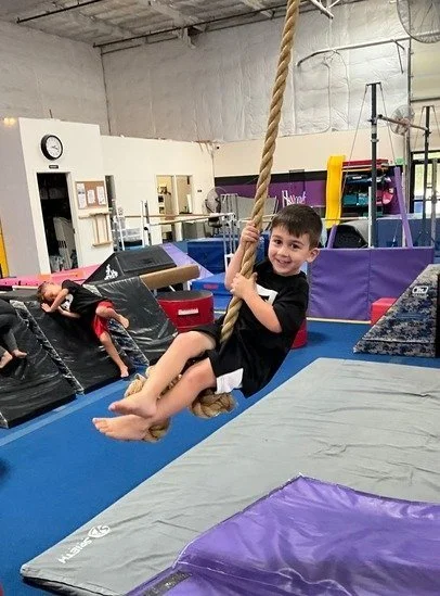 Child smiling while swinging on a rope in an indoor gym.