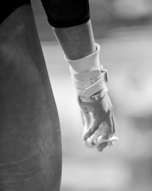 Close-up of an athlete's hand with a wrist brace gripping a sports object, possibly a bar or rope, in a gym setting.