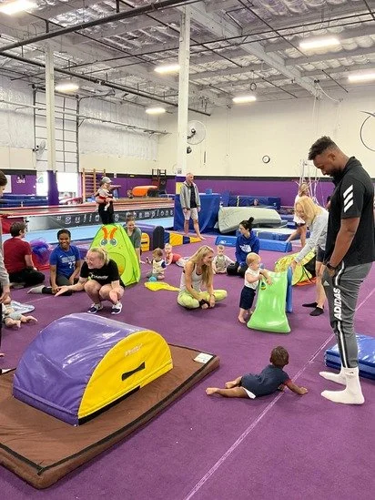 Children and adults in an indoor trampoline park and play area with foam climbing structures and mats.