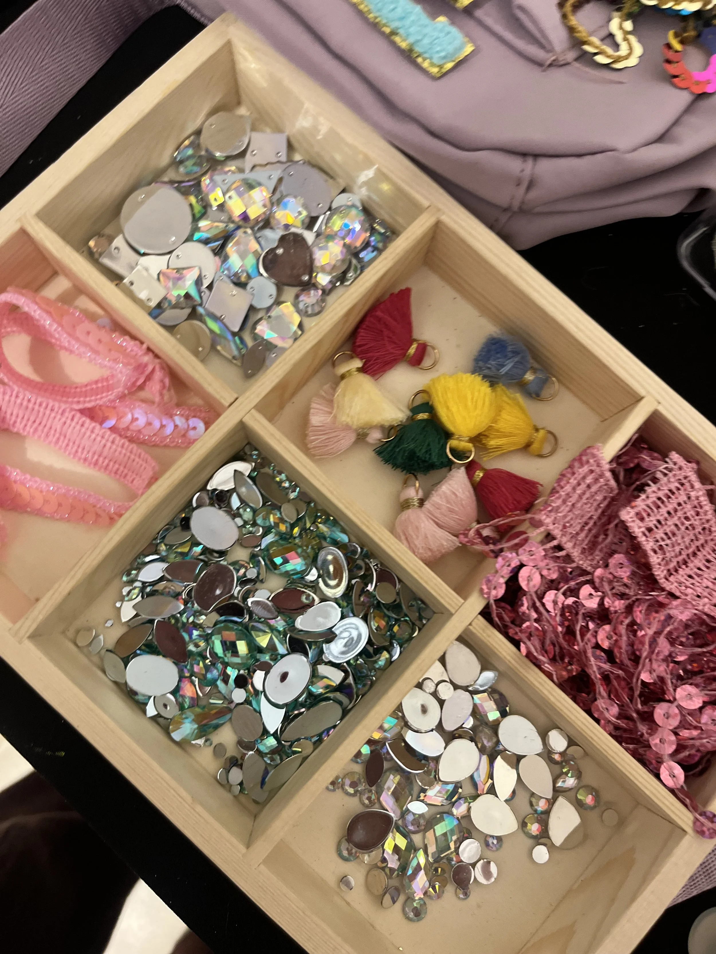 A wooden box containing various shiny, iridescent, and reflective rhinestones, sequins, and decorative embellishments.