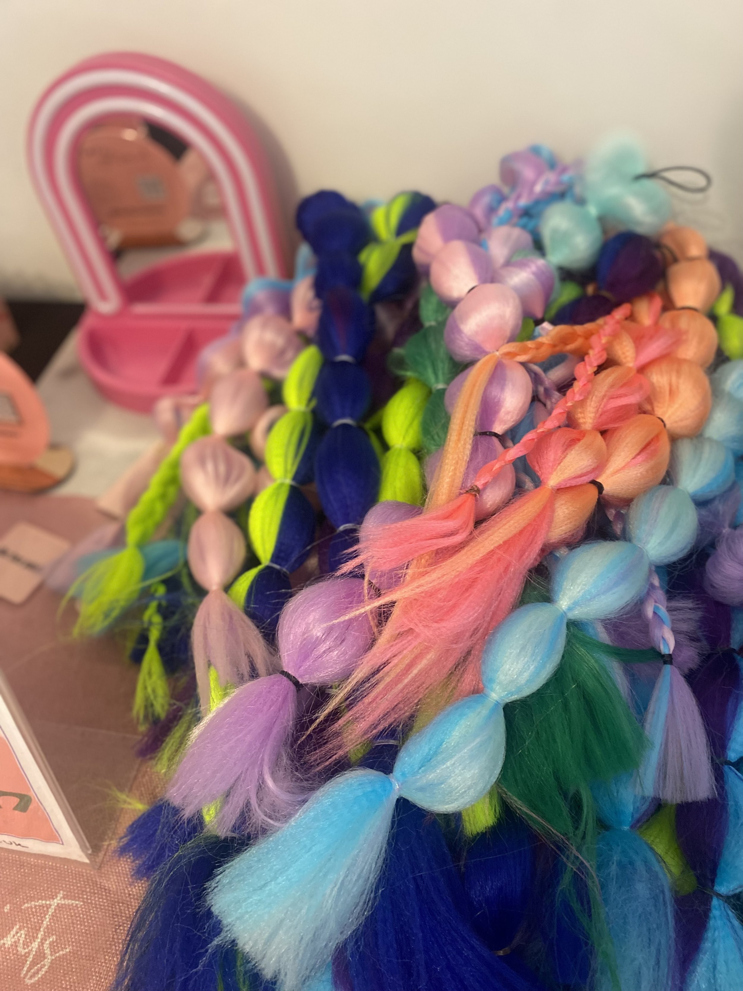 Colorful collection of pastel and neon hair braids and extensions on a display table.