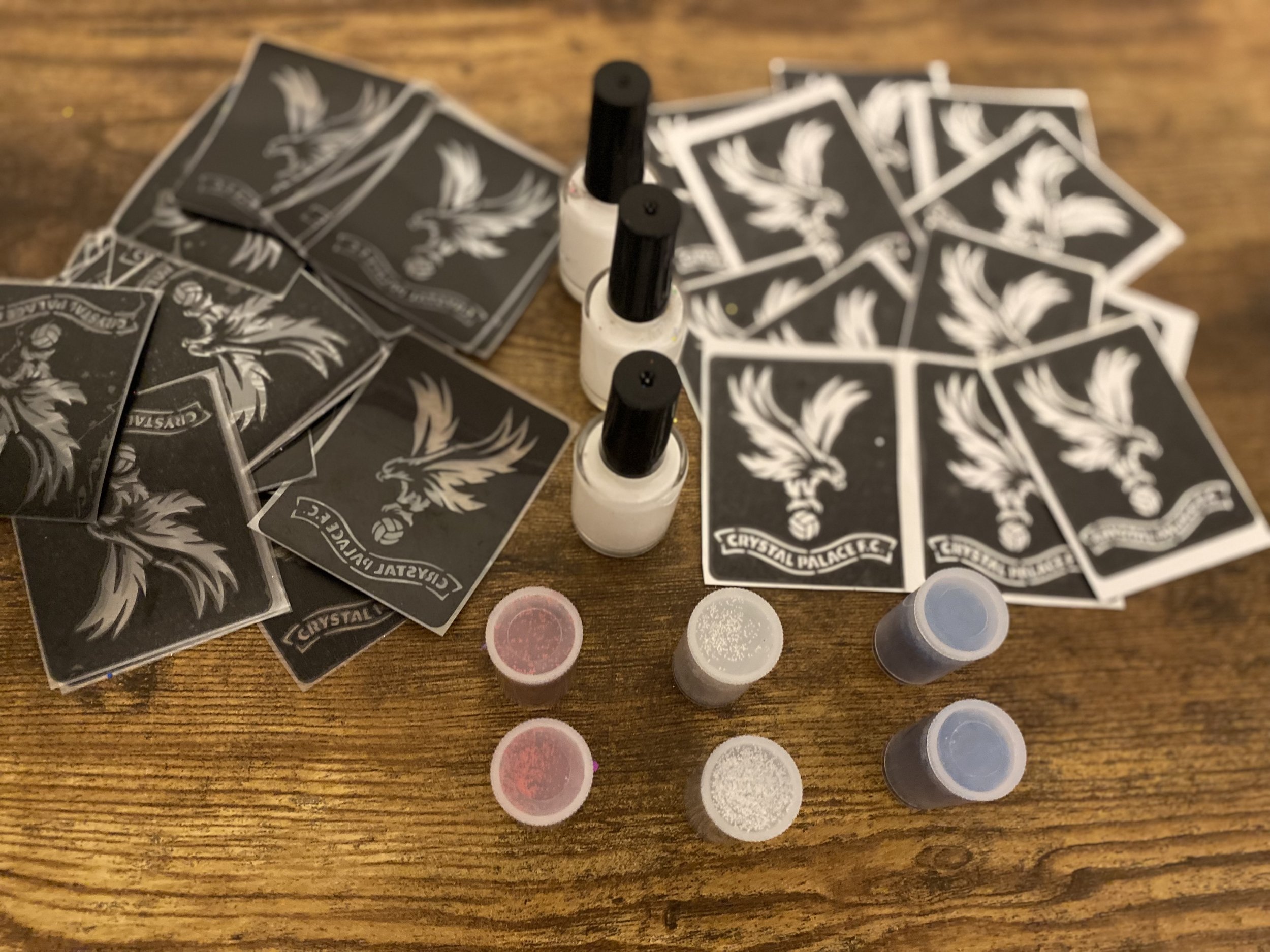A collection of playing cards featuring the Crystal Palace logo, along with bottles of nail polish and small containers of glitter on a wooden surface.