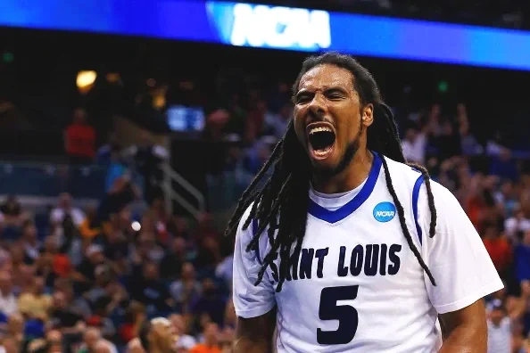 A male athlete with long dreadlocks wearing a Saint Louis jersey with the number 5, shouting passionately during a sports event.