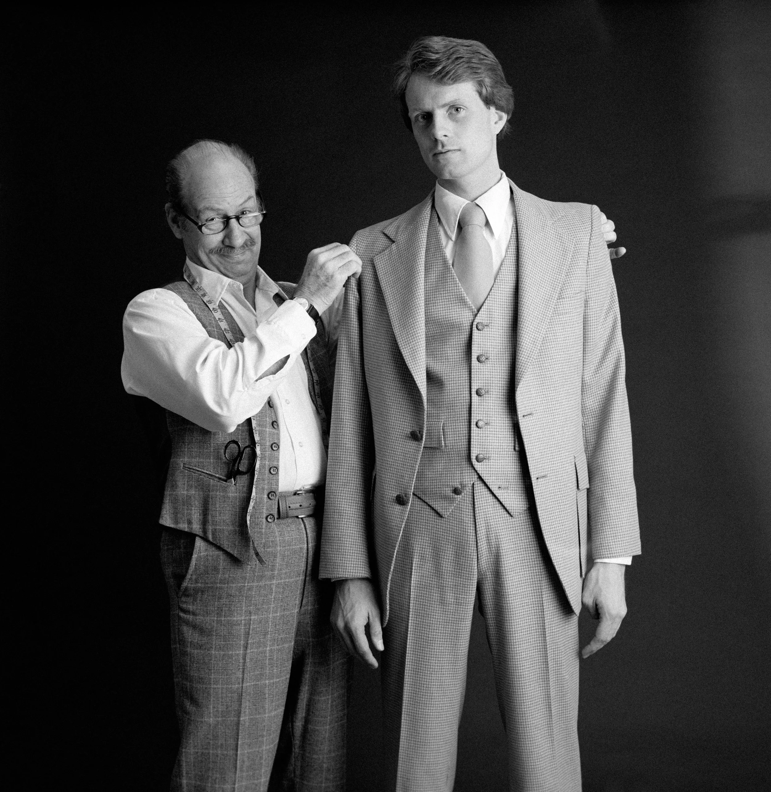 Black and white photo of two people standing between parked semi-trucks on a road.