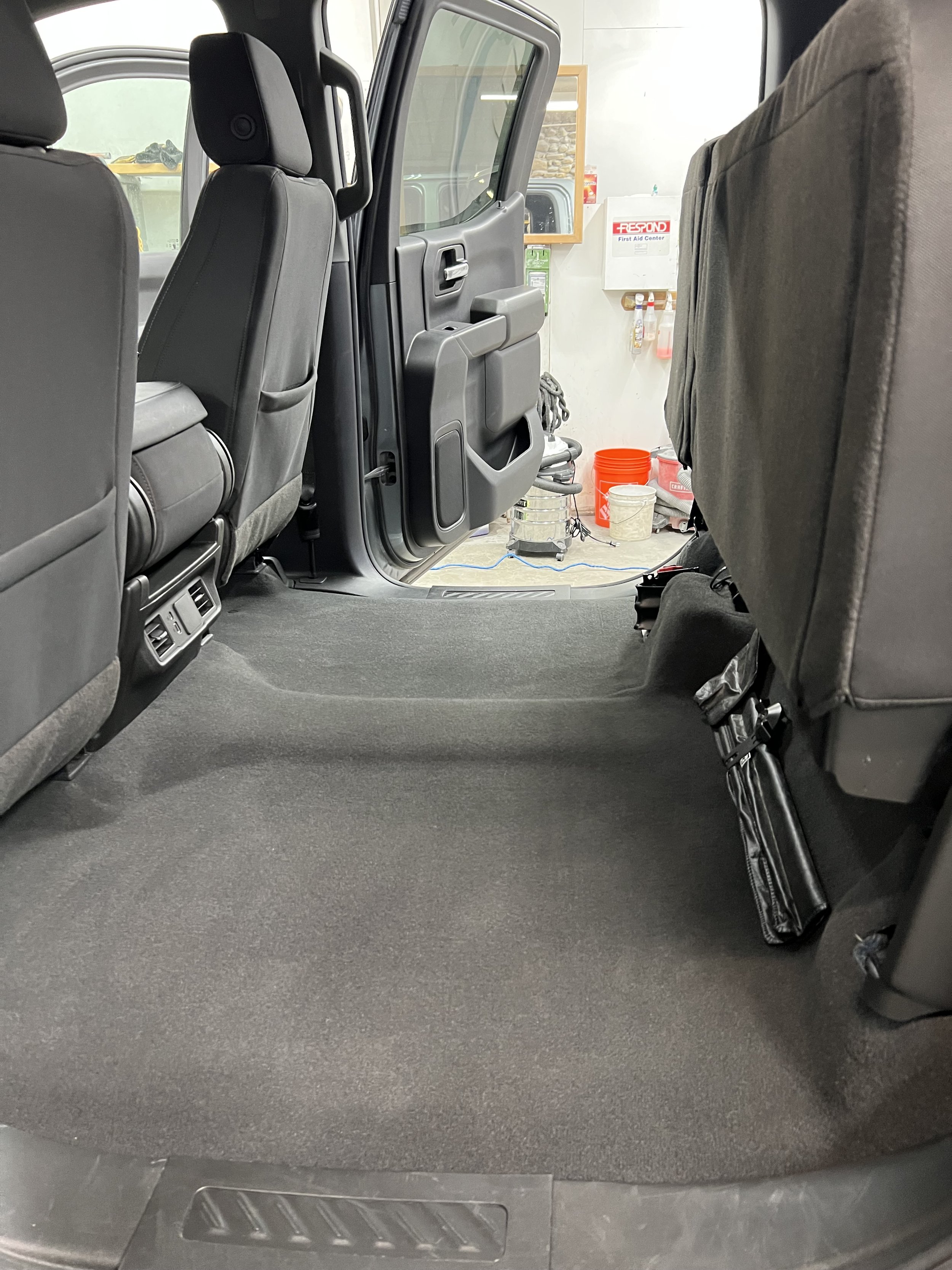 Interior view of a car showing rear seats folded up to reveal extra floor space, with open door and visible vehicle accessories in the background.