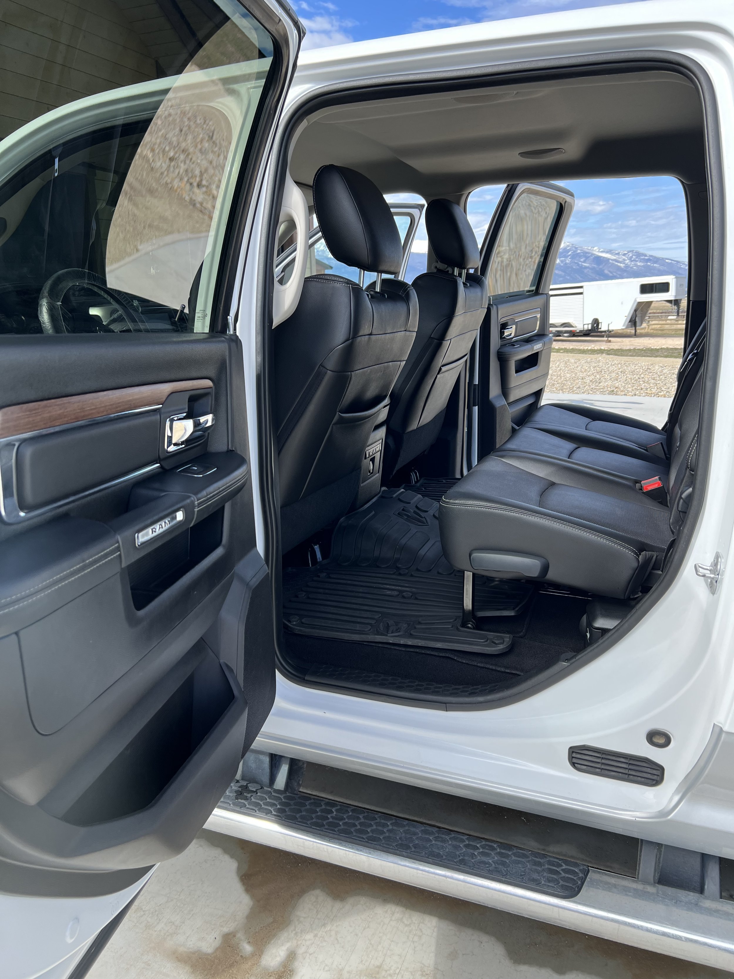 Interior view of a white pickup truck's open rear door, showing black leather seats and a rubber floor mat, with a step bar visible outside.