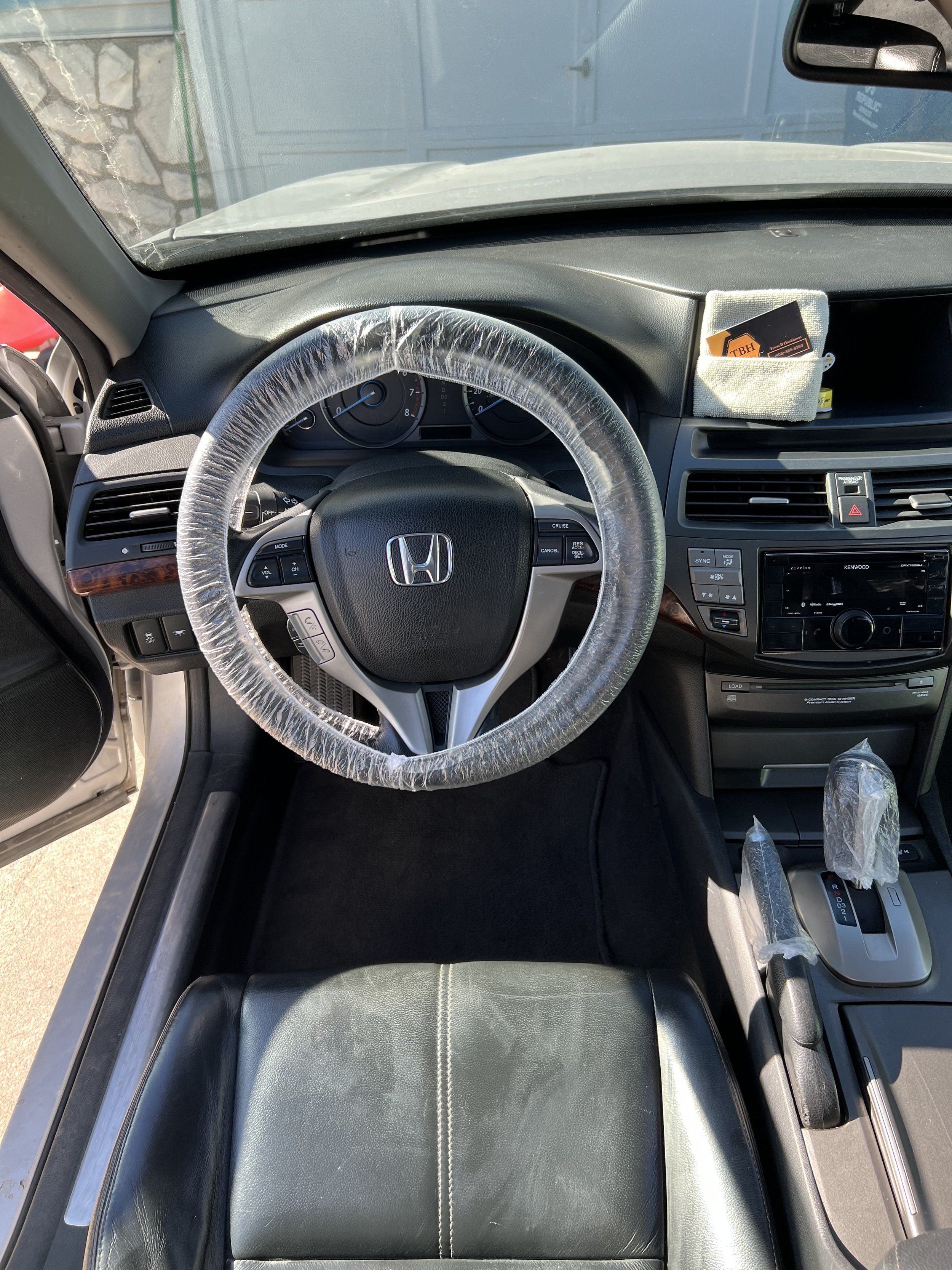 Interior of a car with a covered steering wheel and gear shift, showing Honda logo.