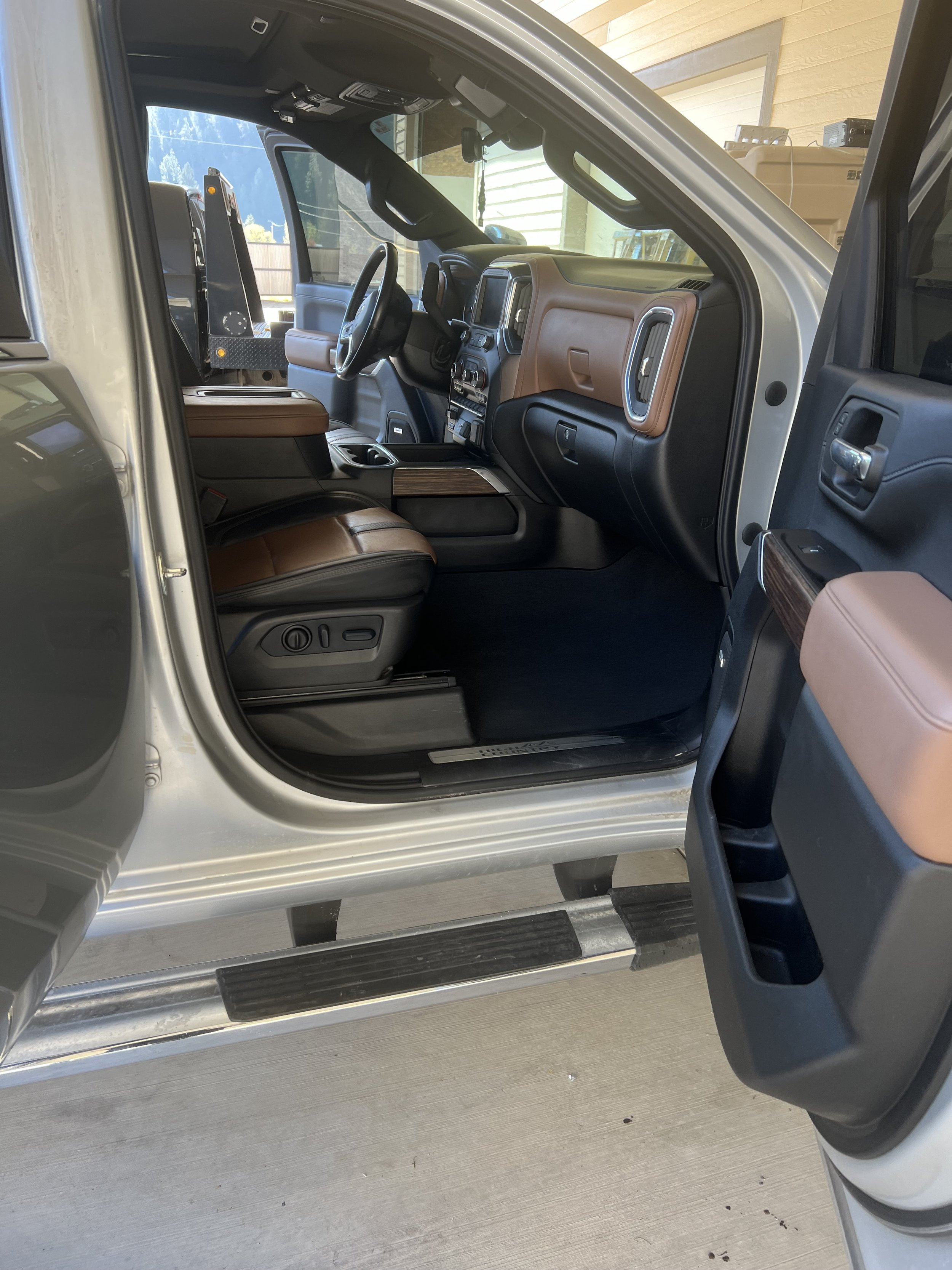 Interior of a pickup truck with brown leather seats and black dashboard, showing the driver's side open door.