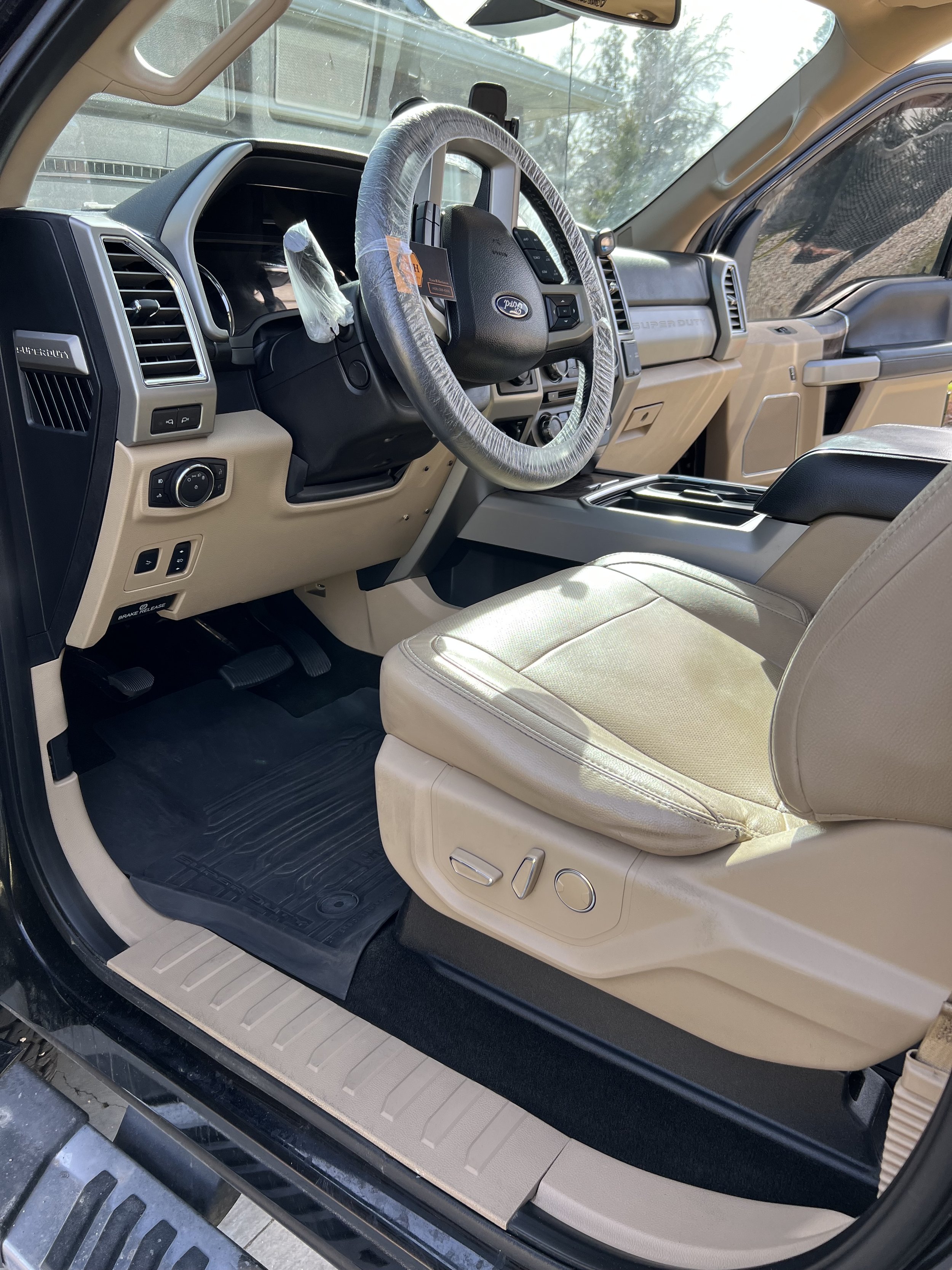 Interior of a Ford vehicle featuring a leather driver seat, wrapped steering wheel, dashboard, and door panel. Visible vehicle controls and console area.
