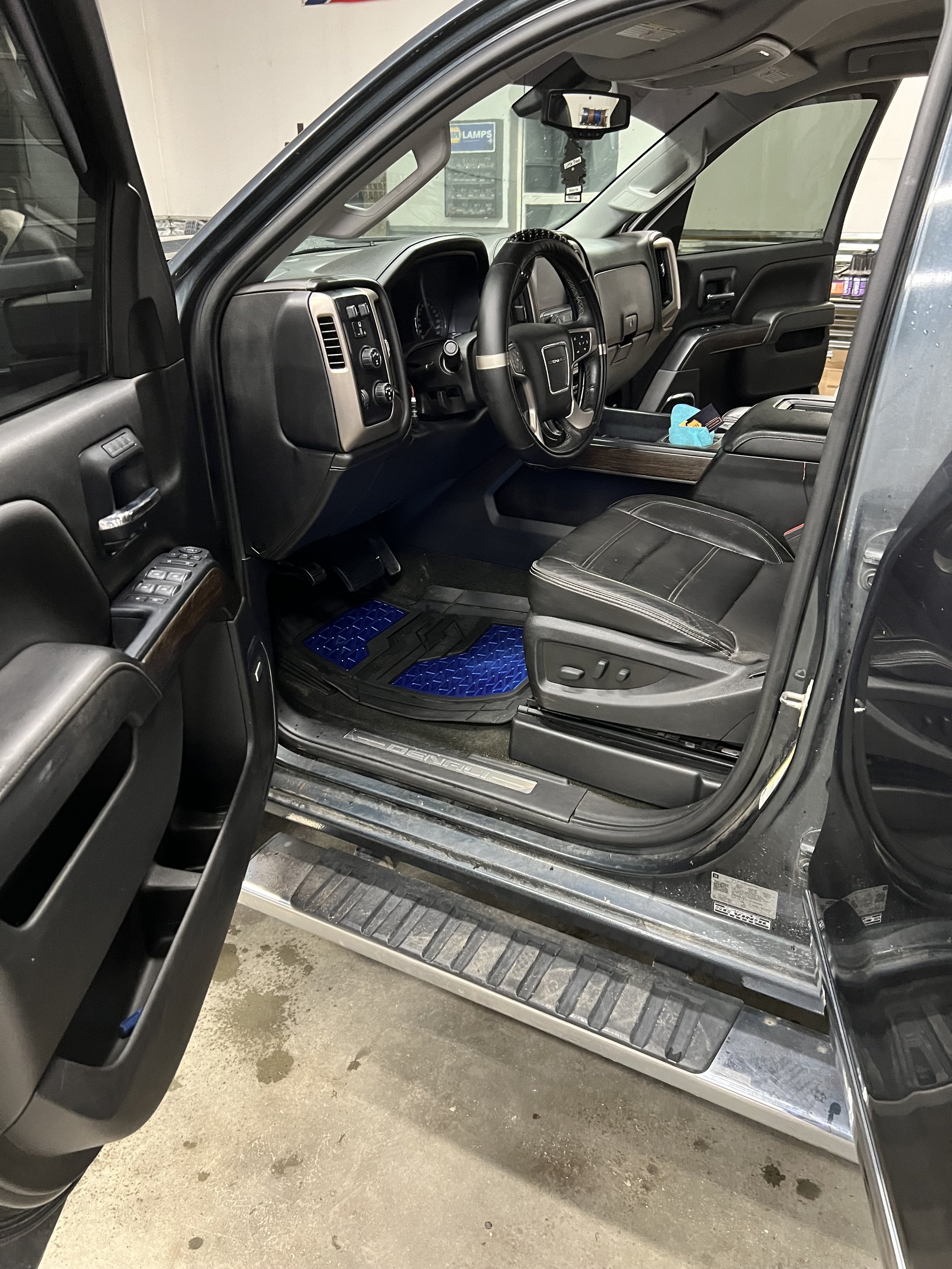 Interior view of a black SUV or truck, showing front seats, steering wheel, dashboard, and driver-side door open.