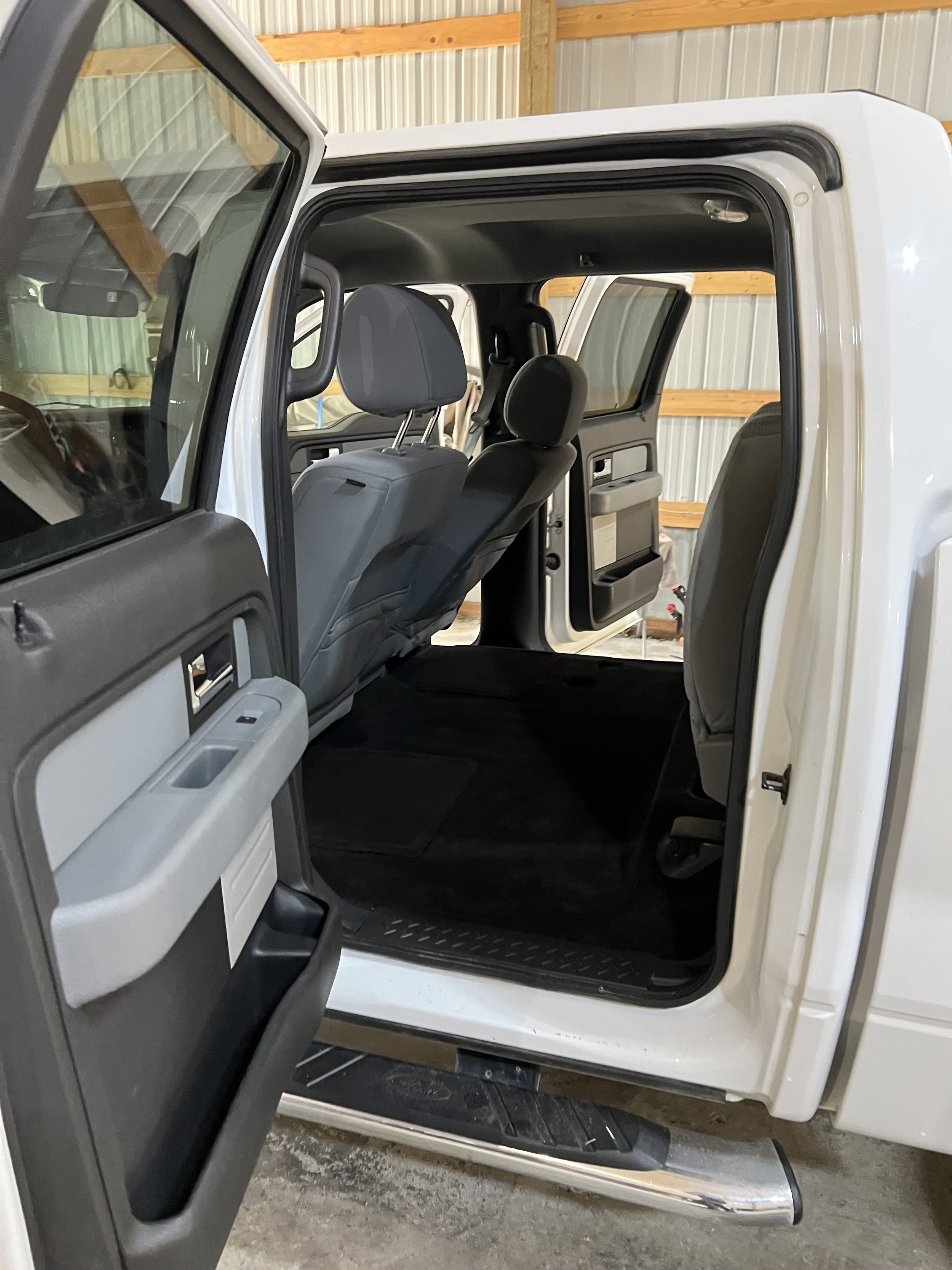 Interior view of the backseat area of a white pickup truck with open rear door, showing gray seating and black floor mats.
