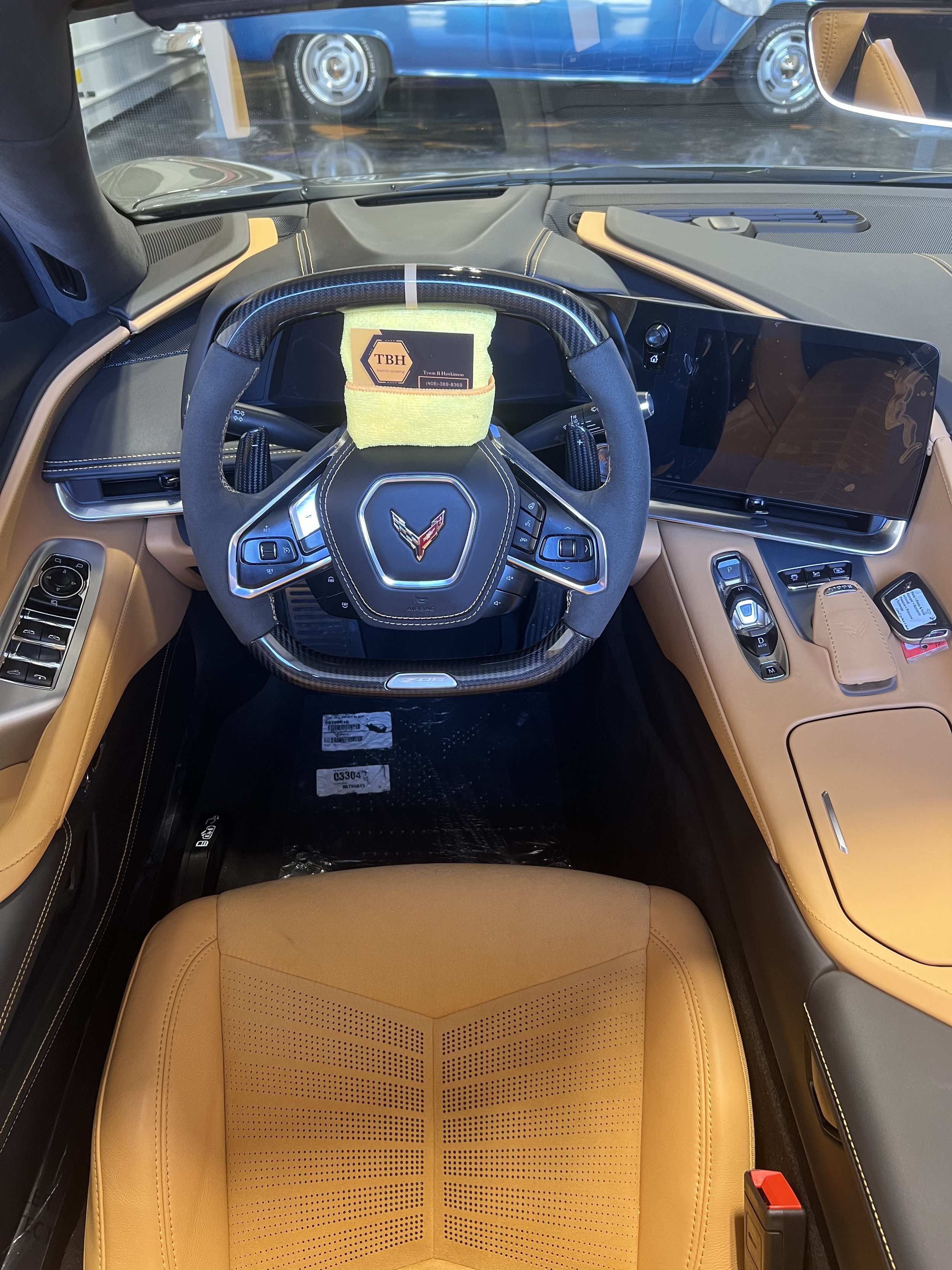 Interior view of a sports car featuring a black steering wheel with a logo, tan leather seats, digital dashboard, and control panels.