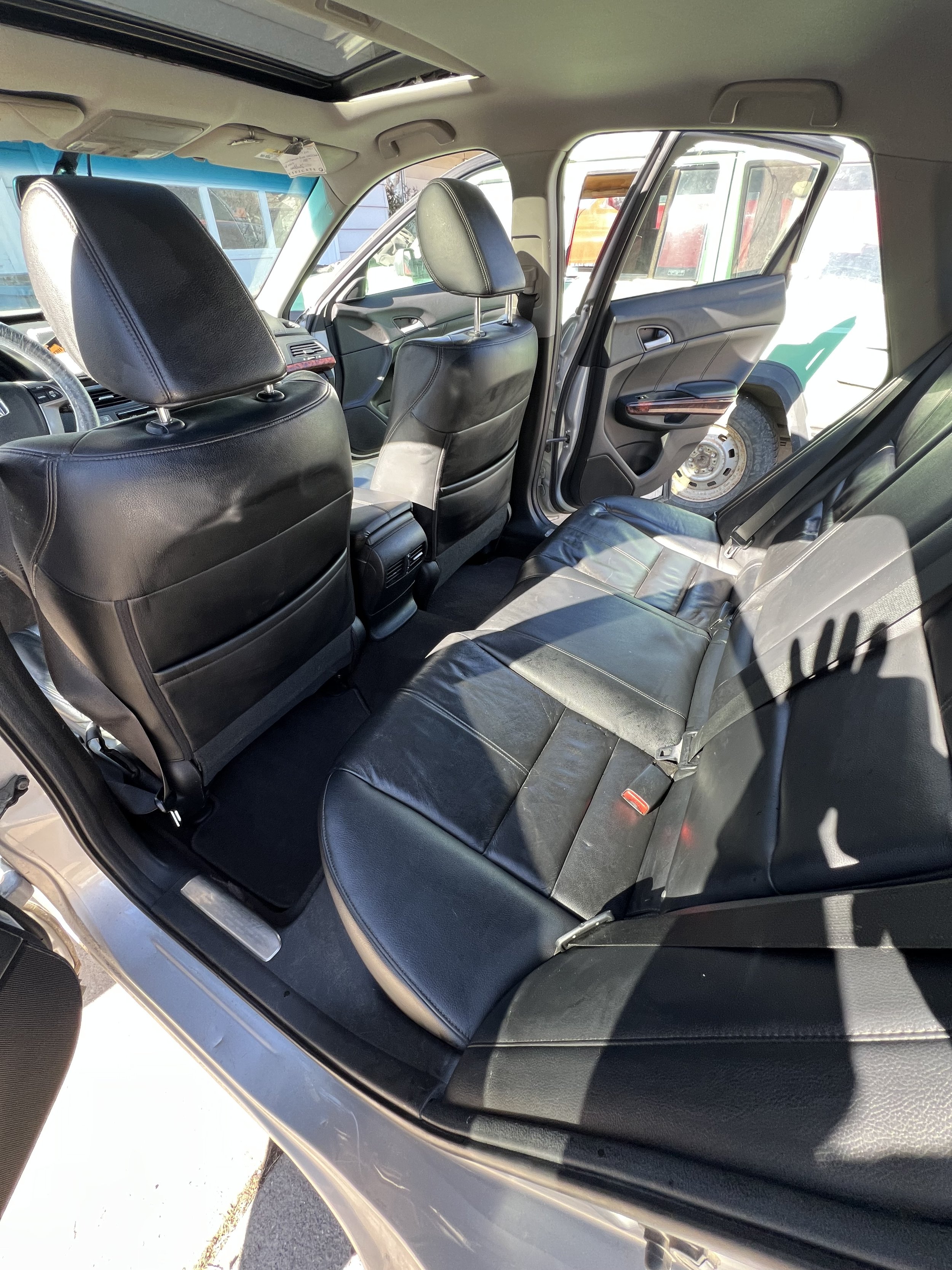 Interior of a car with black leather seats and a sunroof, showing the back and front seats with both doors open.