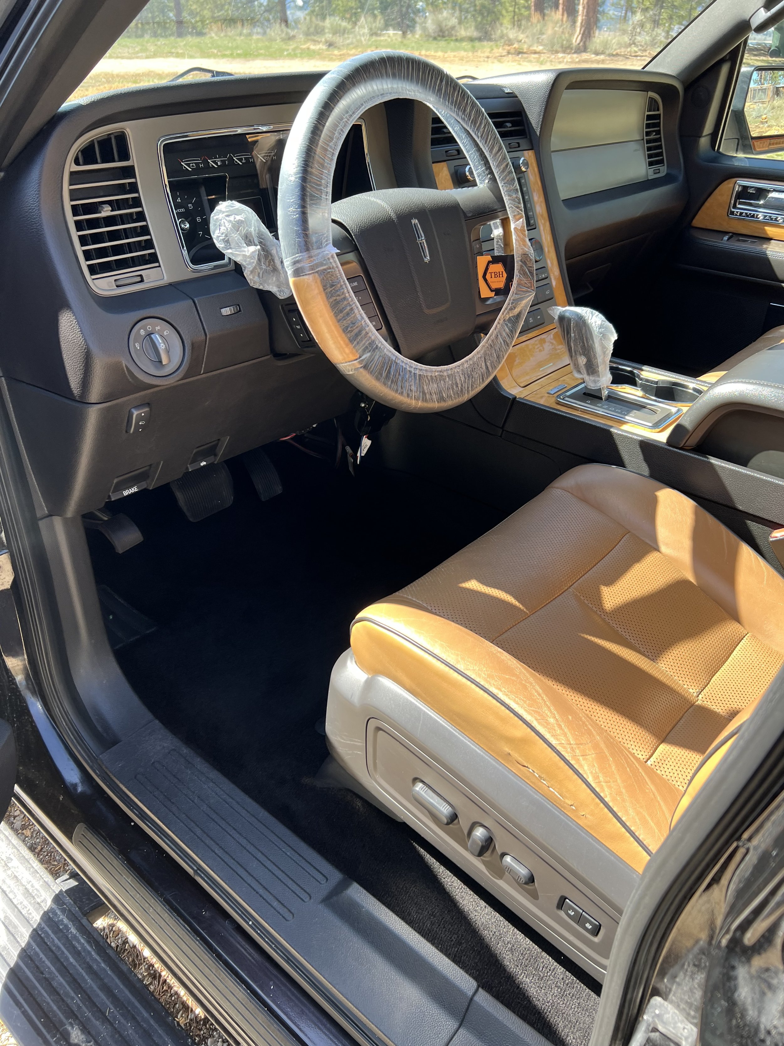Interior of a luxury vehicle with a leather seat, wrapped steering wheel, and a console displaying various controls.