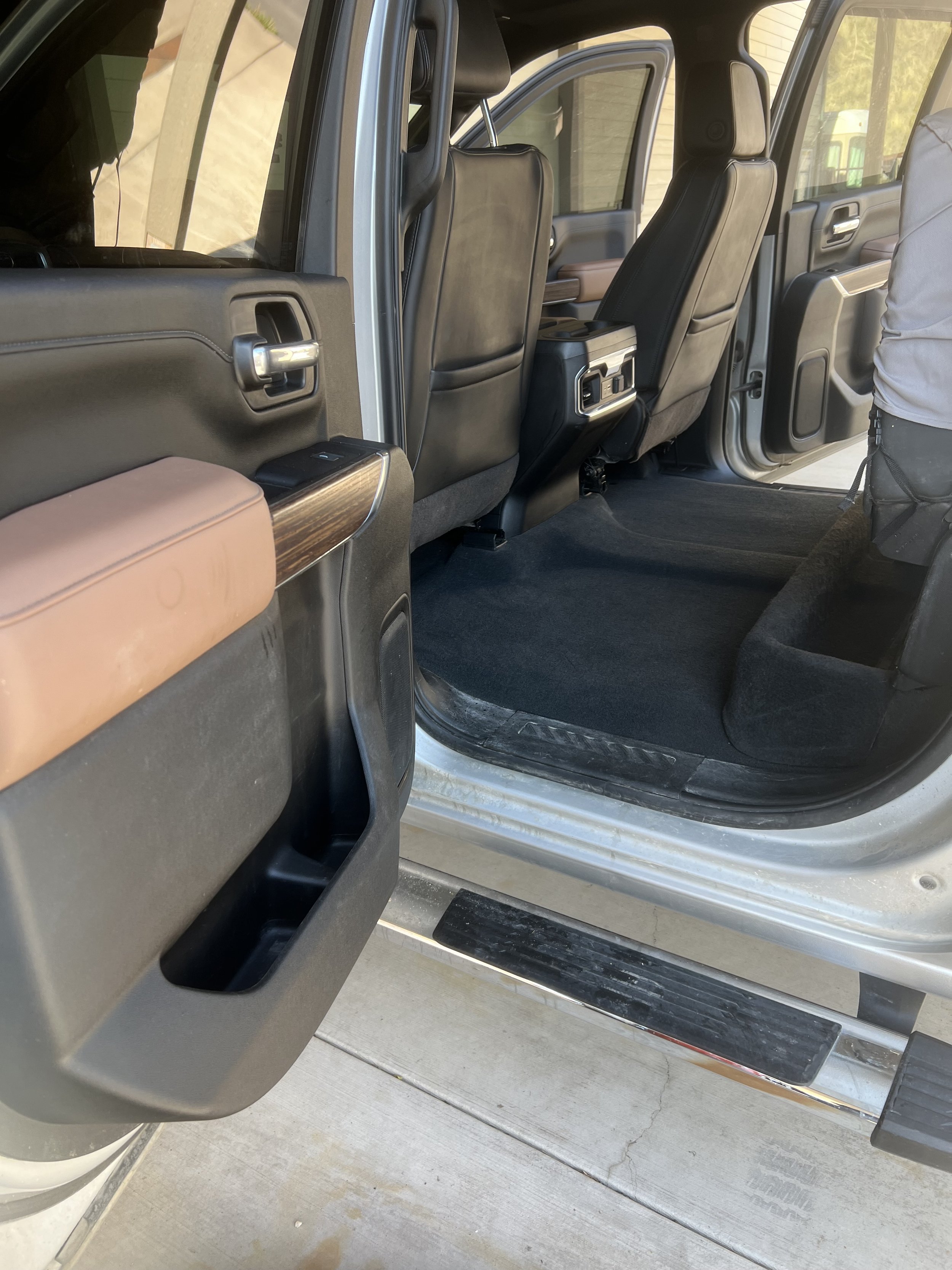 Interior of a parked vehicle with open rear door, showing black leather seats, floor mats, and a step bar outside the door.