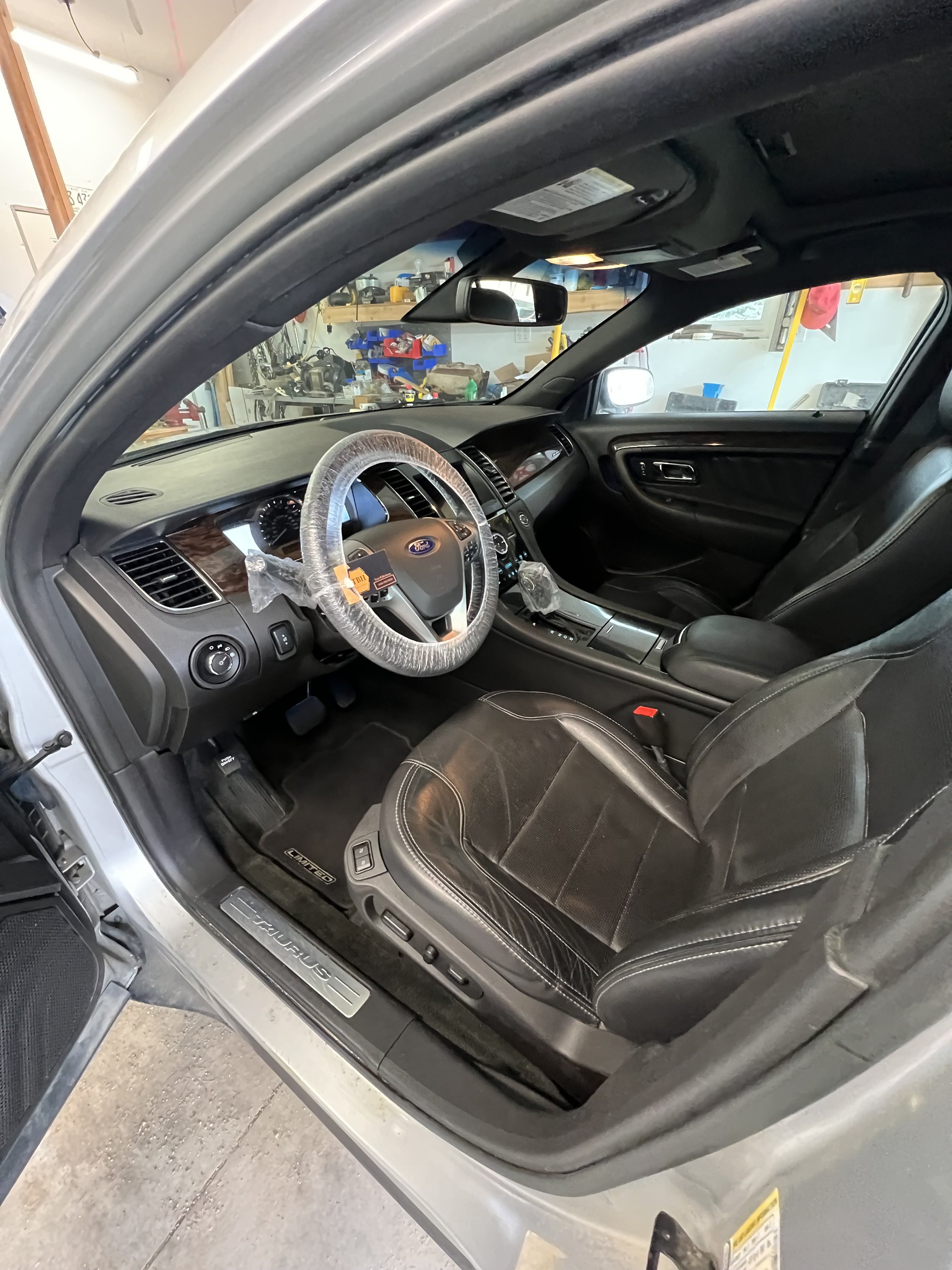Interior of a Ford Taurus showing leather seats and steering wheel covered with protective plastic.