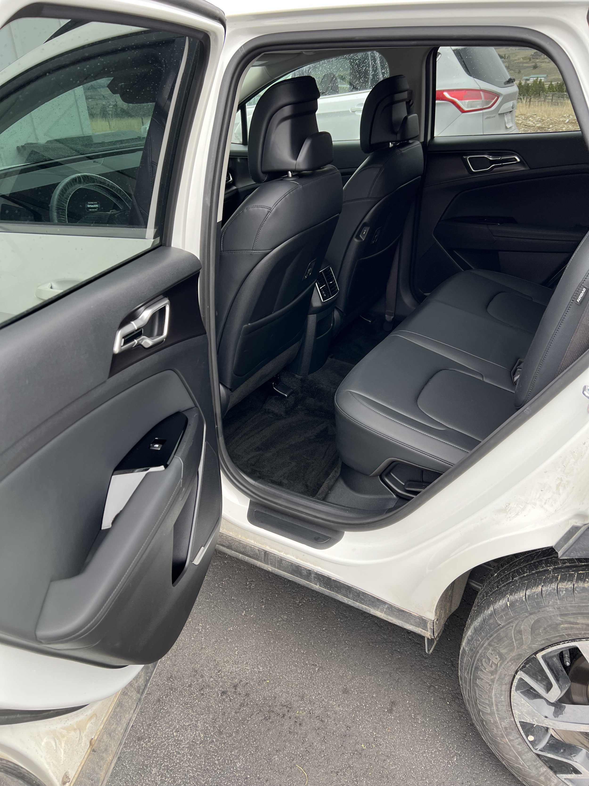 Open rear door of a car with black leather interior and visible back seats.