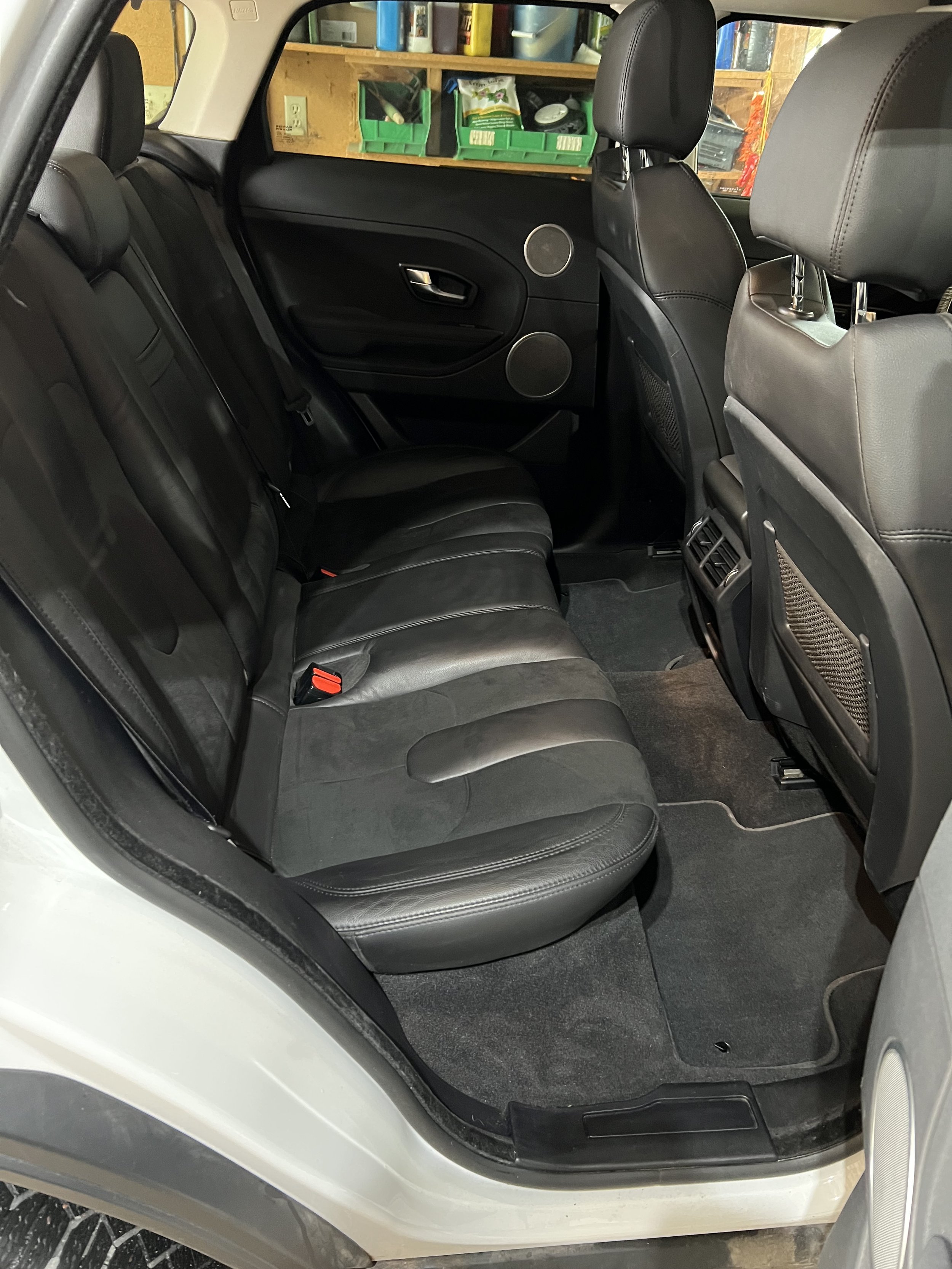 Interior of a car's back seat with black leather upholstery and storage bins on the back of the front seats.