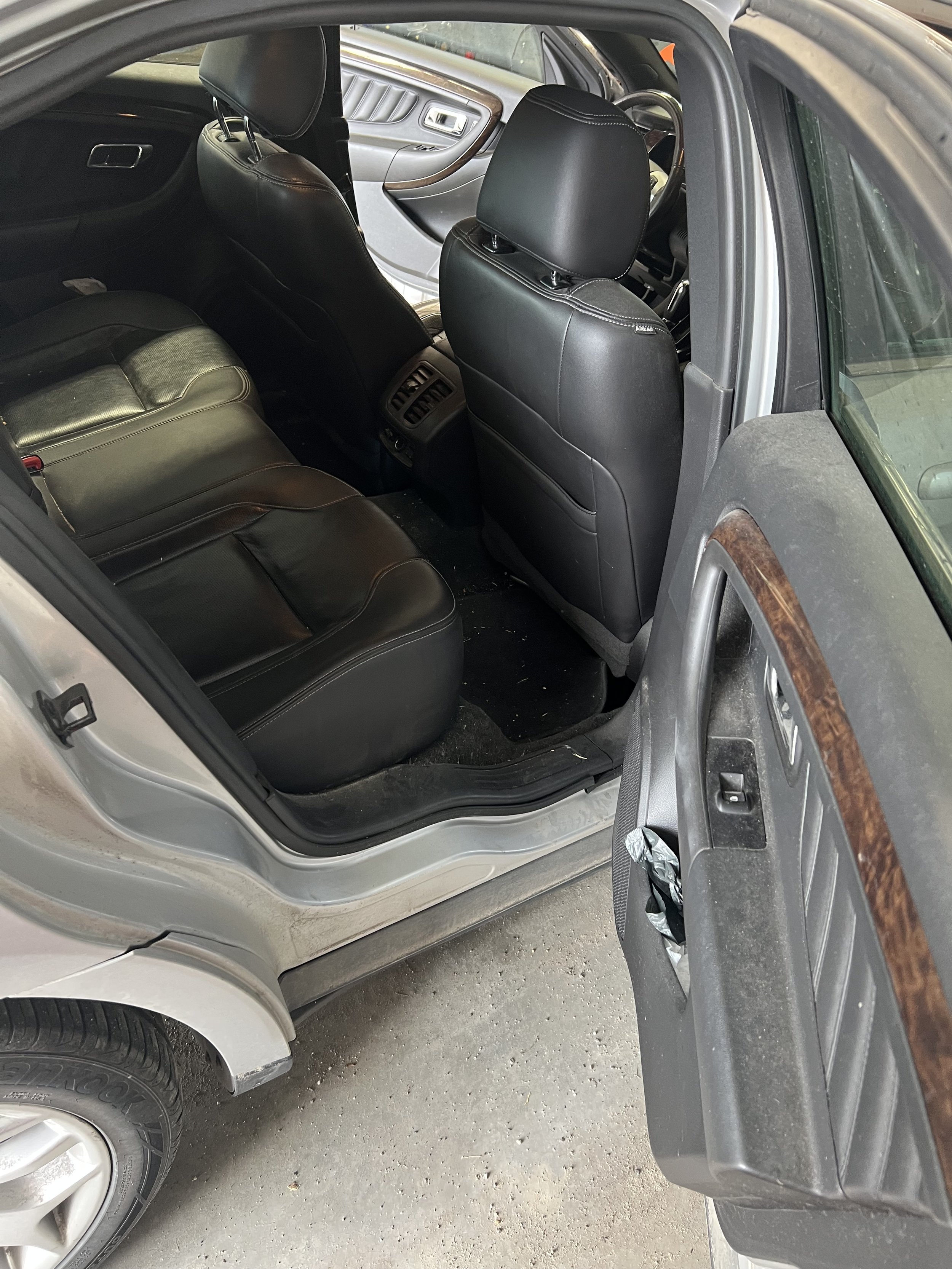 Interior view of an open car door showing the backseat with black leather upholstery.