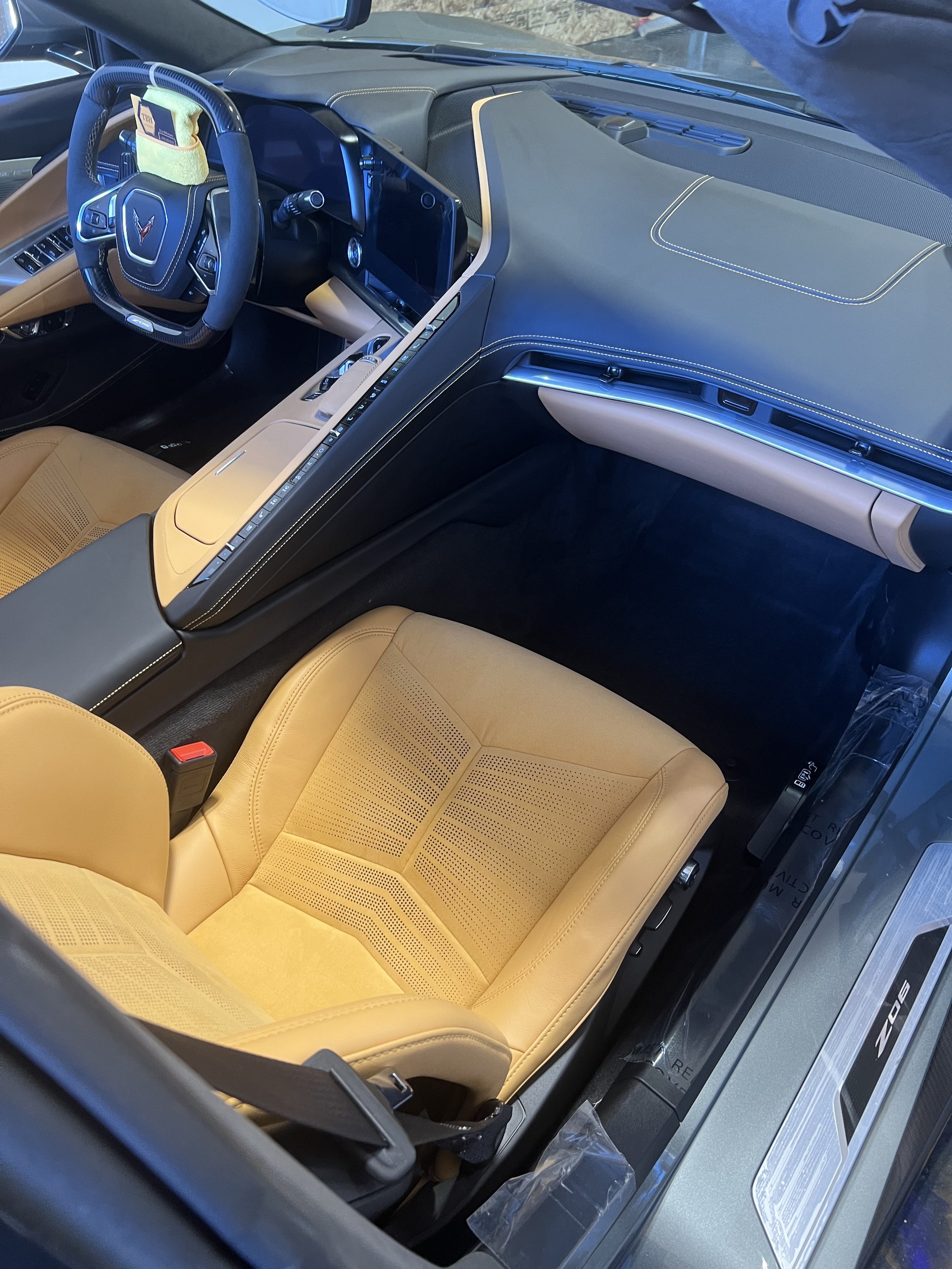 Interior view of a car's cockpit featuring tan leather seats, a steering wheel with a cover, and a modern dashboard with digital displays and controls.