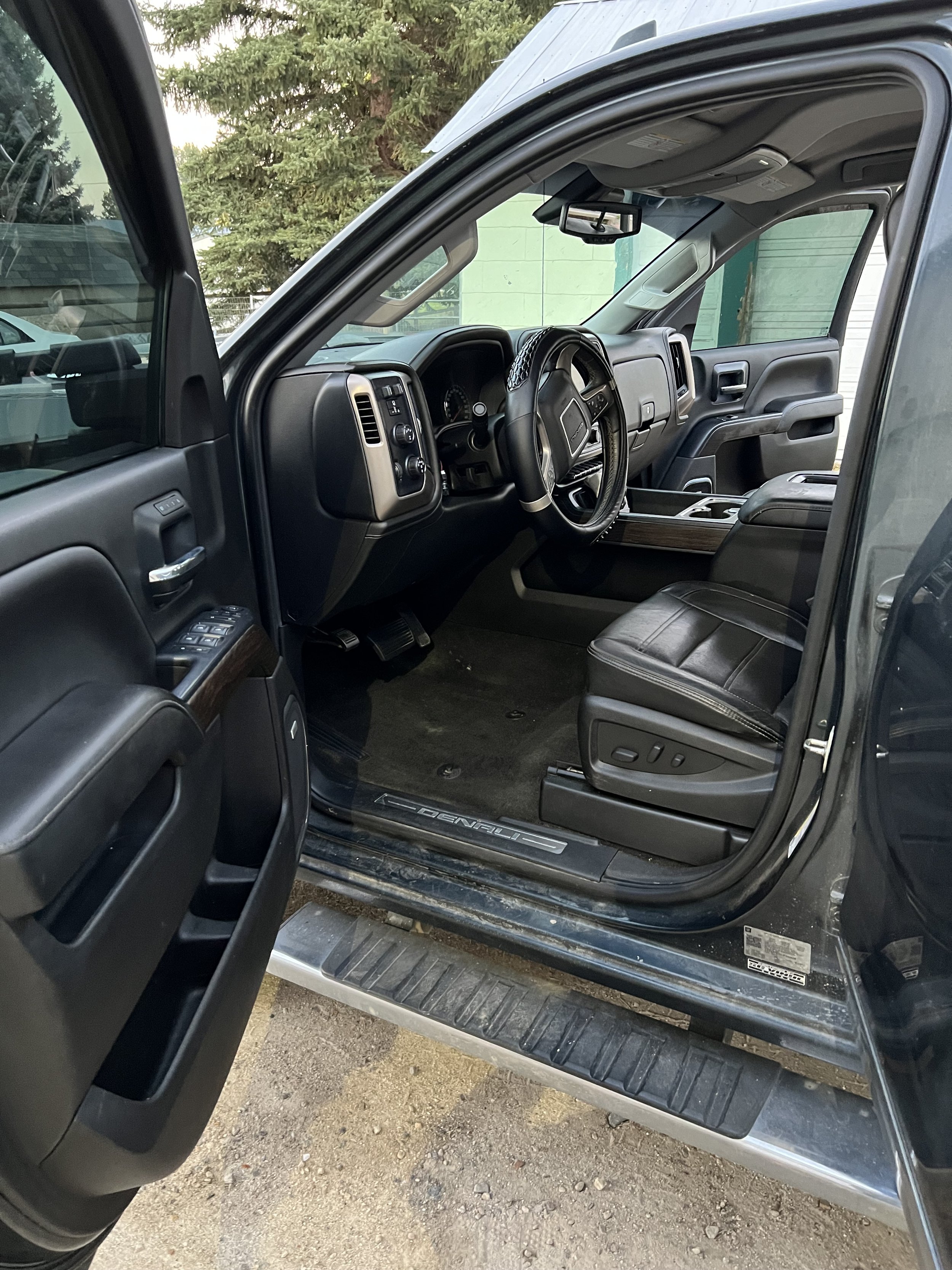 Interior of a truck with open driver-side door; features a steering wheel, dashboard, and black leather seating.