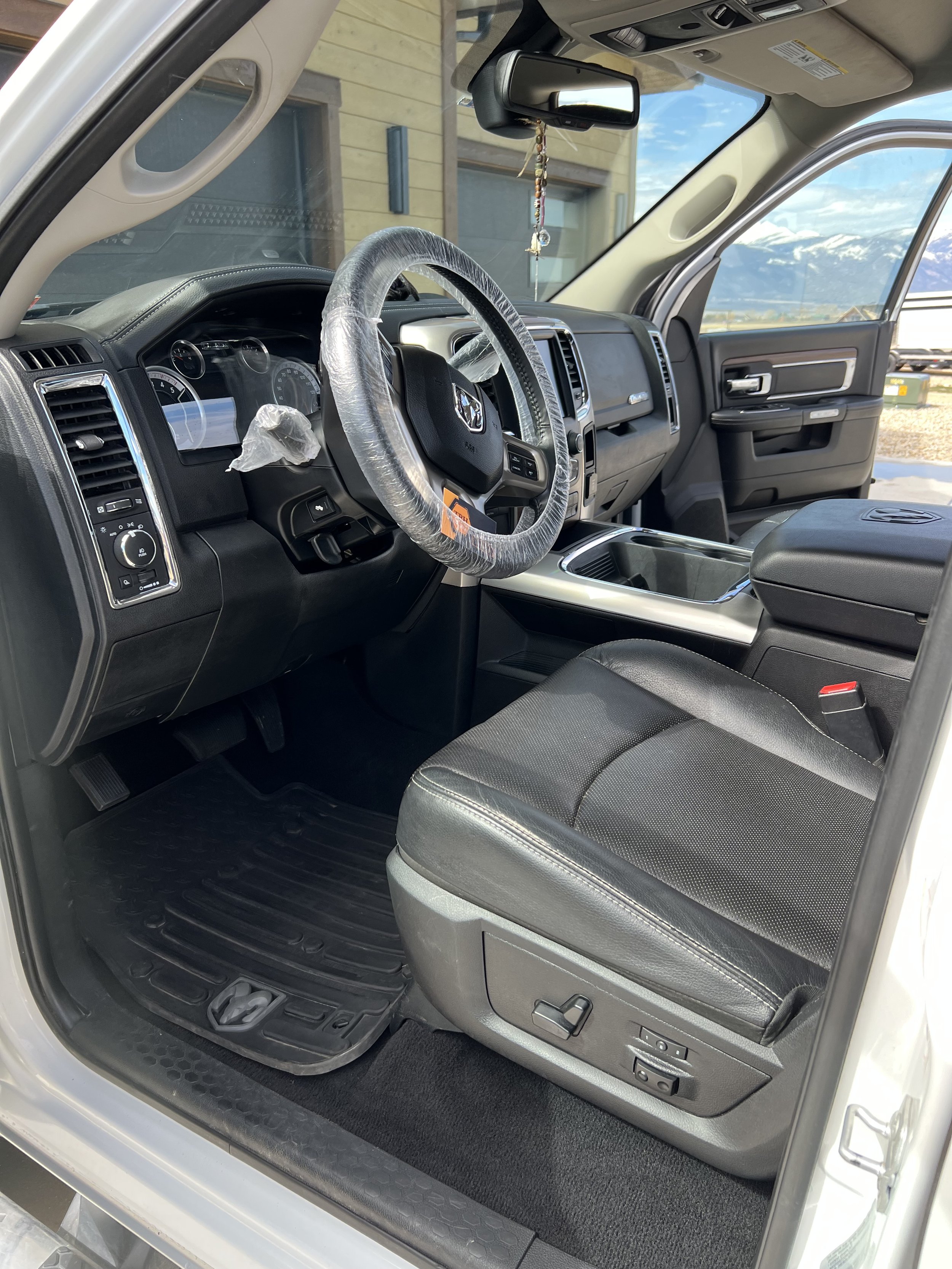Interior of a pickup truck with a wrapped steering wheel, black leather seats, dashboard controls, and view of the outside landscape through the open driver's side door.