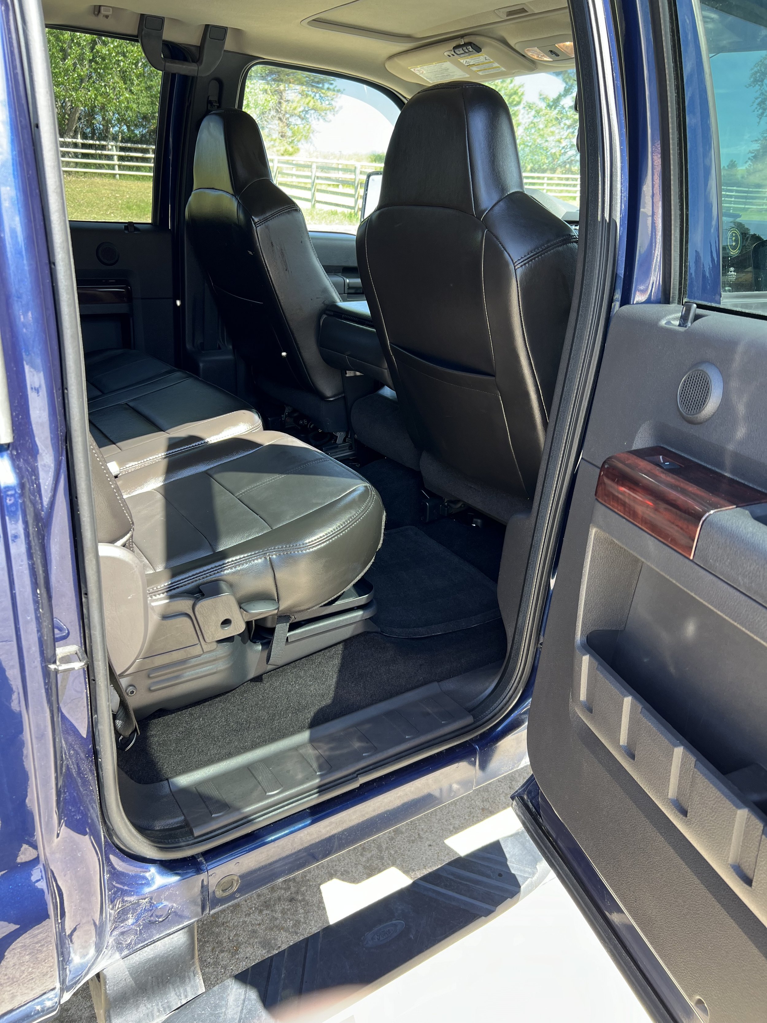 Rear view of the interior of a vehicle with black leather seats, open door, and visible outdoor scenery.
