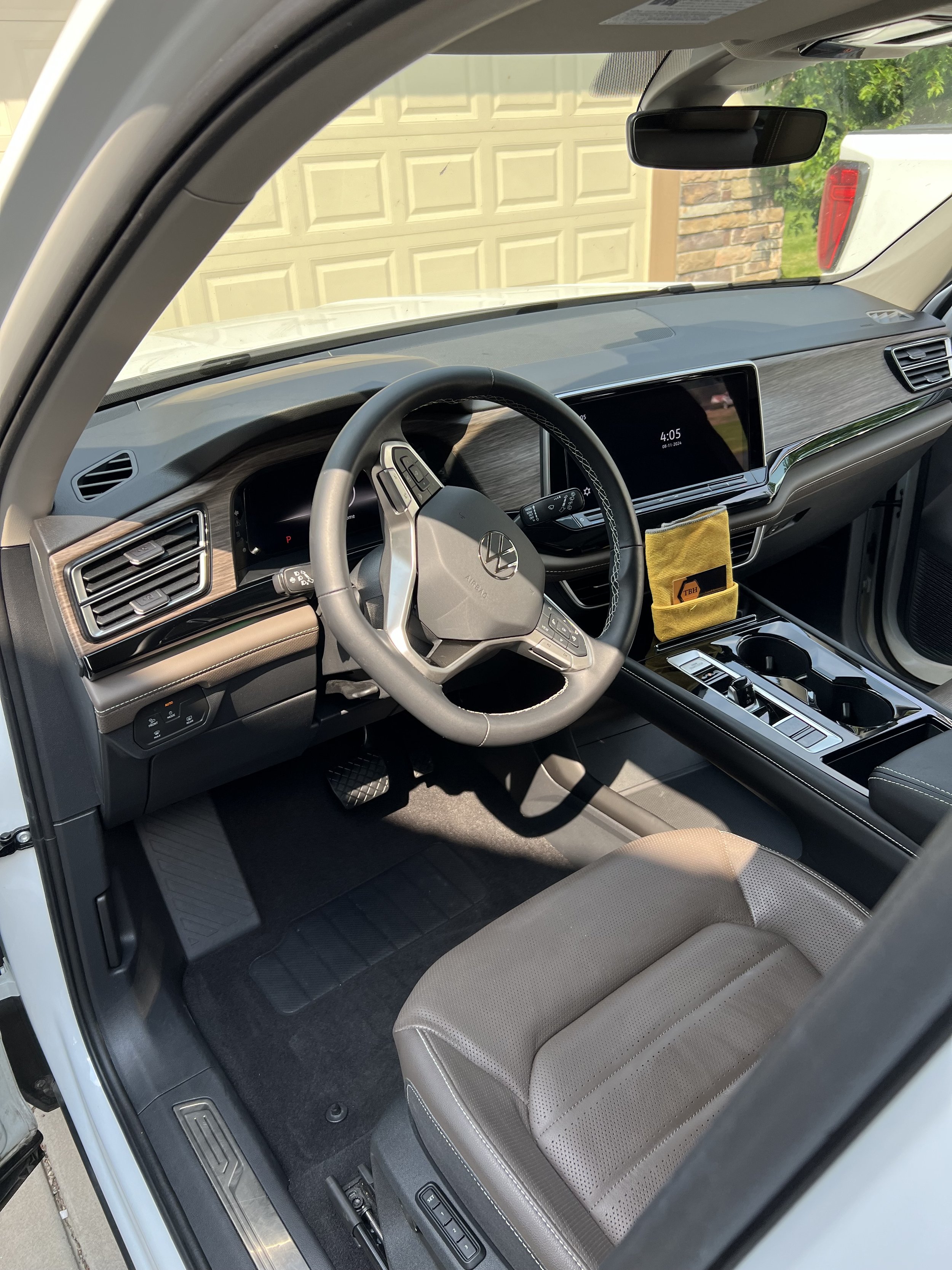 Interior of a modern car's front cabin featuring a steering wheel, digital display, leather seat, and center console with cup holders.