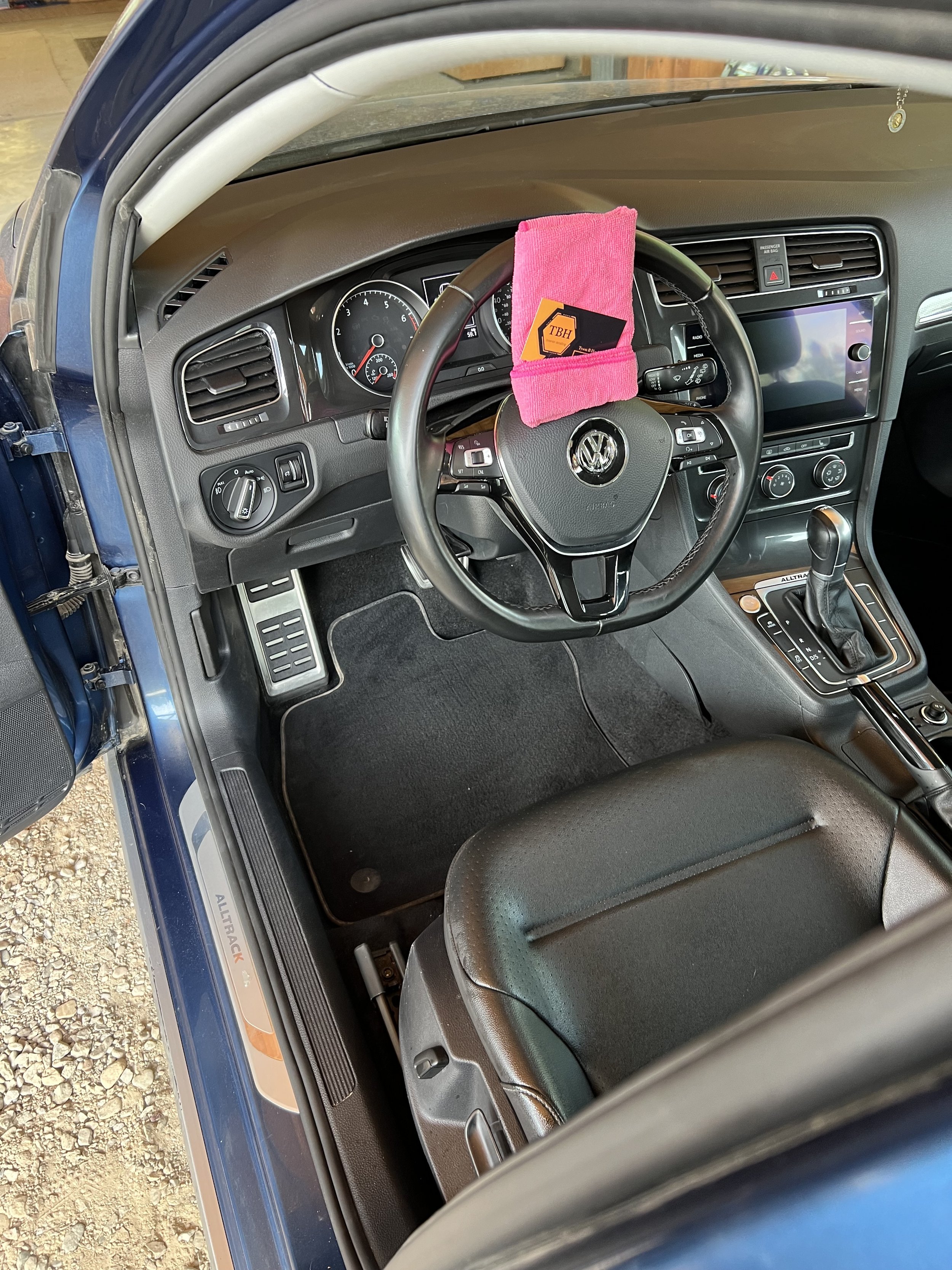 Car interior focused on the driver's seat and steering wheel with a pink cloth and cards on top.