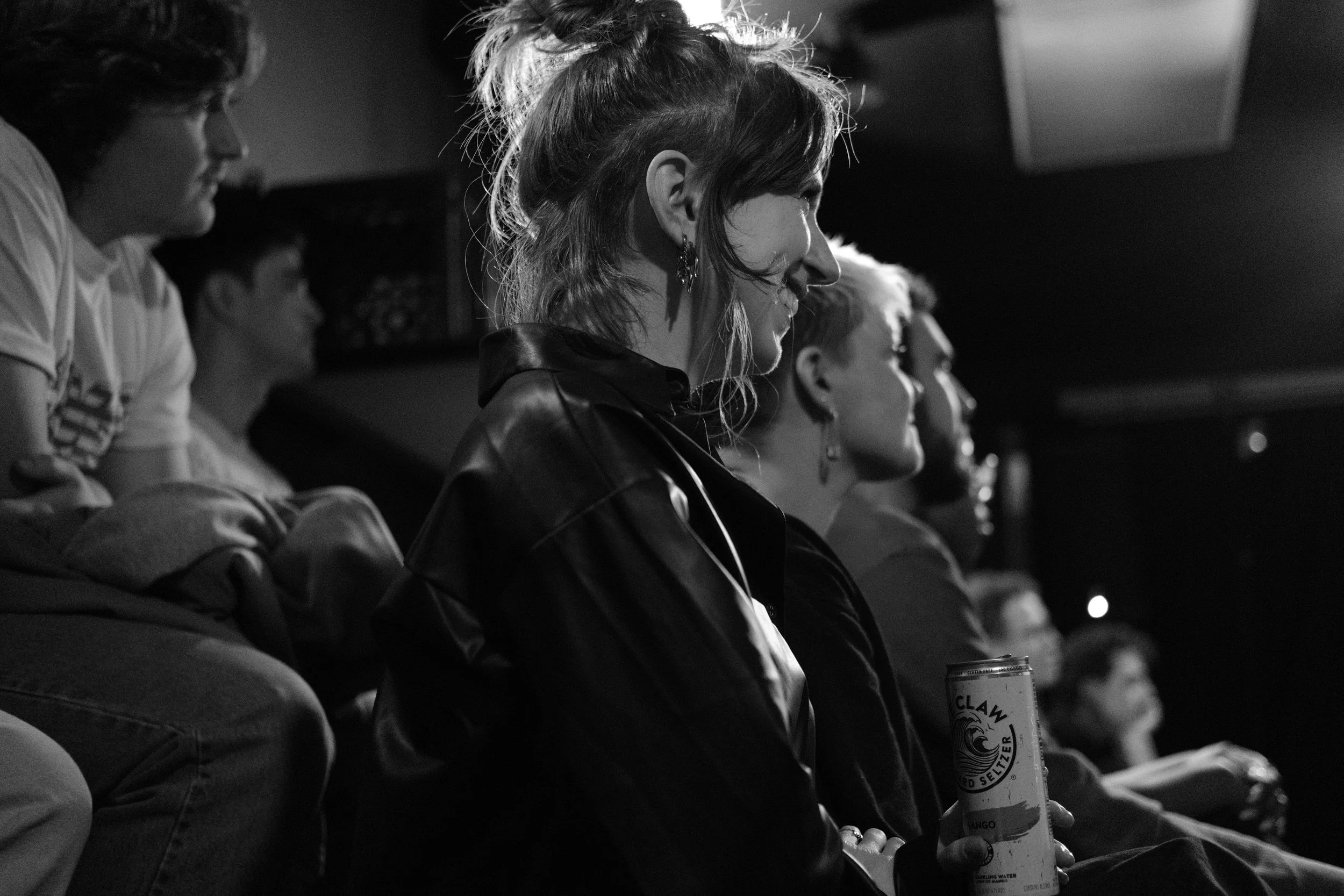 Black and white photo of people sitting closely in a dimly lit room, one person holding a canned beverage.