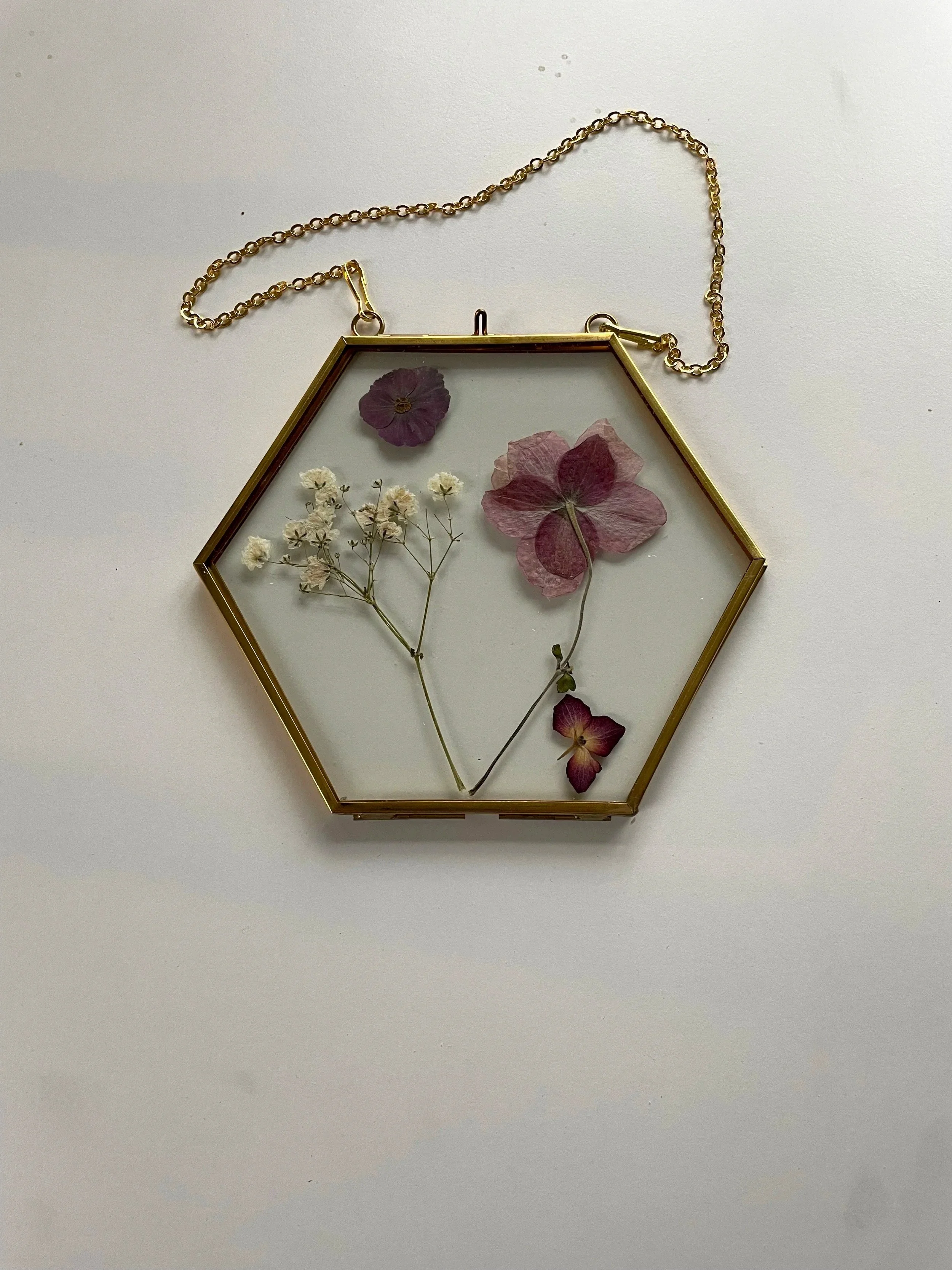 Hexagonal glass jewelry box with dried pink and purple flowers and a chain handle.