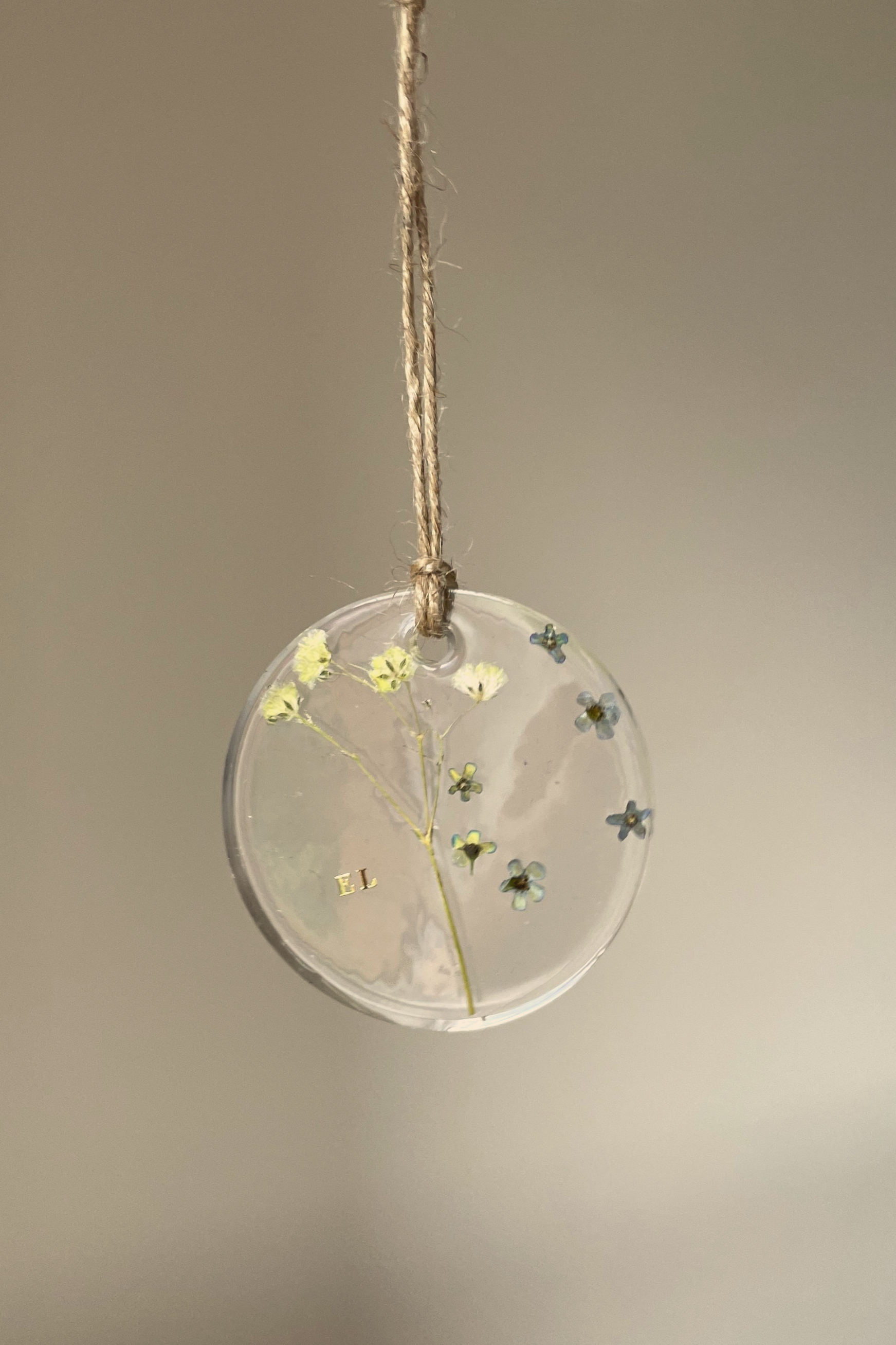 A clear round resin ornament with tiny flowers and a small branch inside, hanging from a piece of twine.