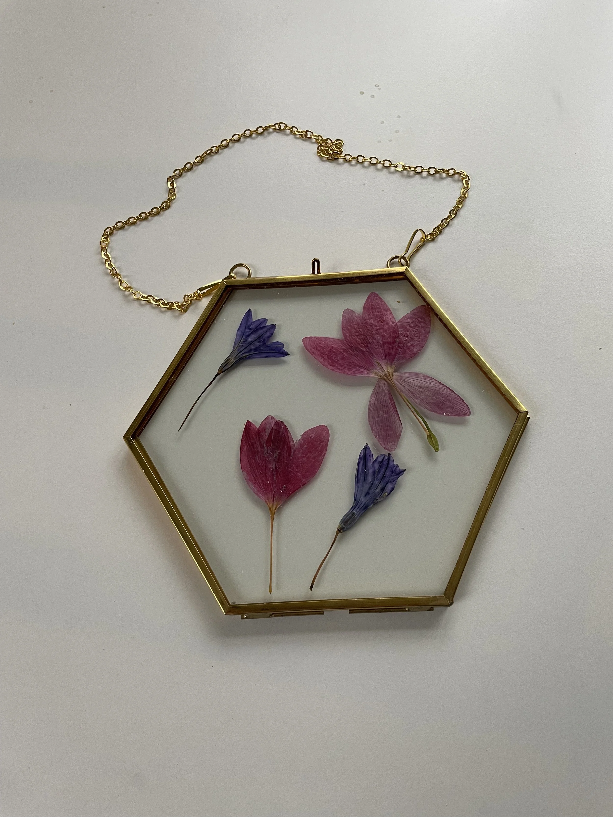 Hexagon-shaped glass pendant with dried pink and purple flowers inside, attached to a gold chain.