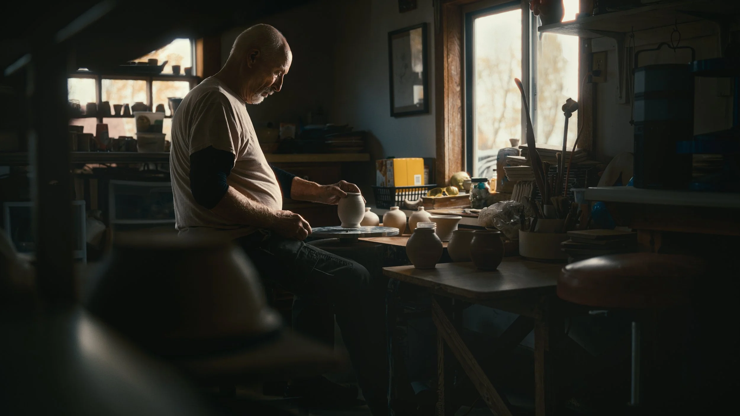 Wide-angle, moody environmental commercial portrait of a man working on pottery in a studio in Hamilton, MI