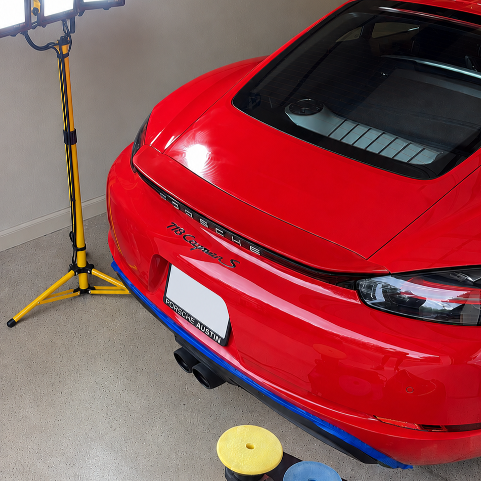 Red Porsche 718 Cayman S in a garage near a yellow studio light and a green and yellow stool.