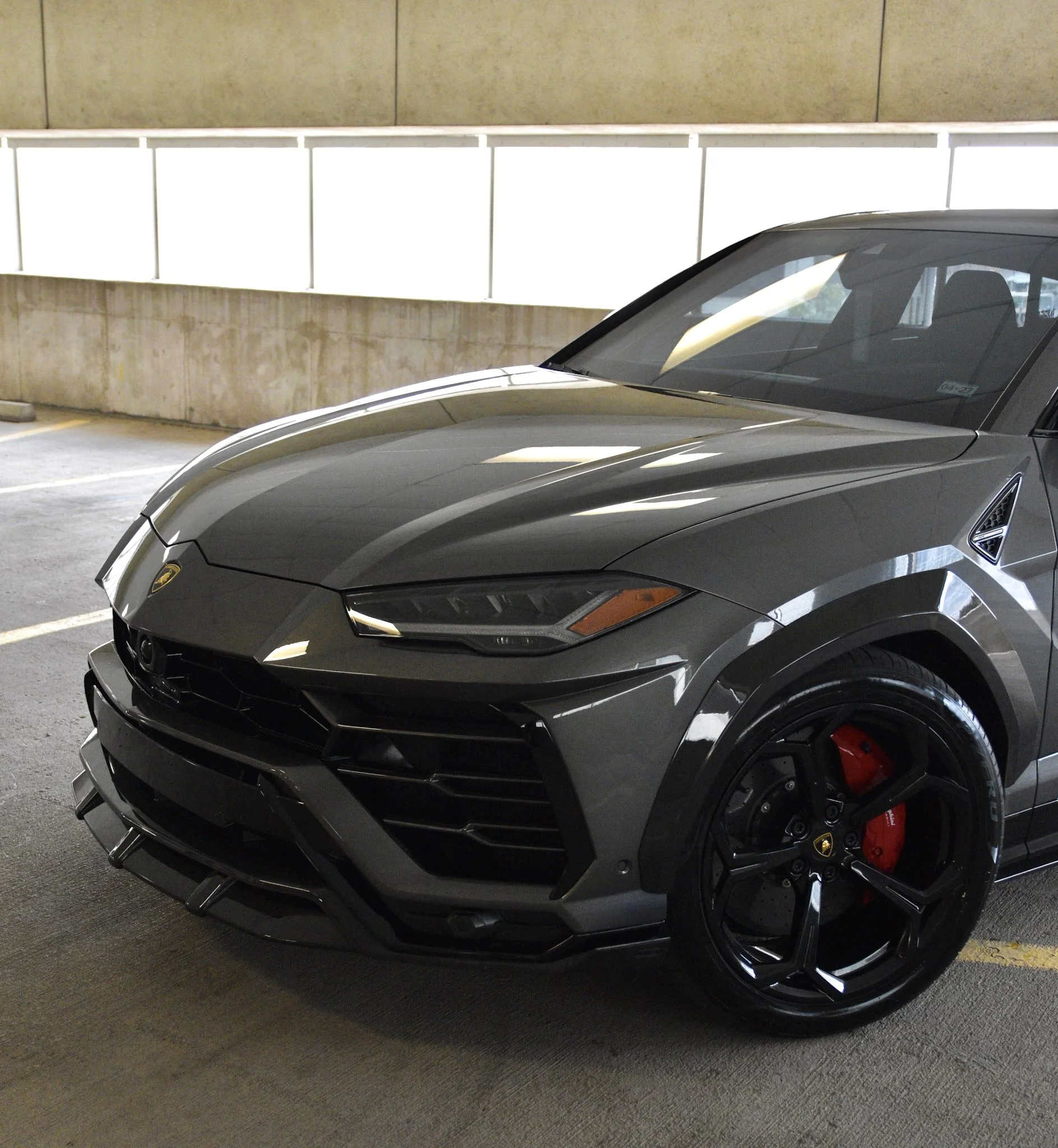 A gray luxury sports car, likely a Lamborghini, parked in an indoor parking garage.