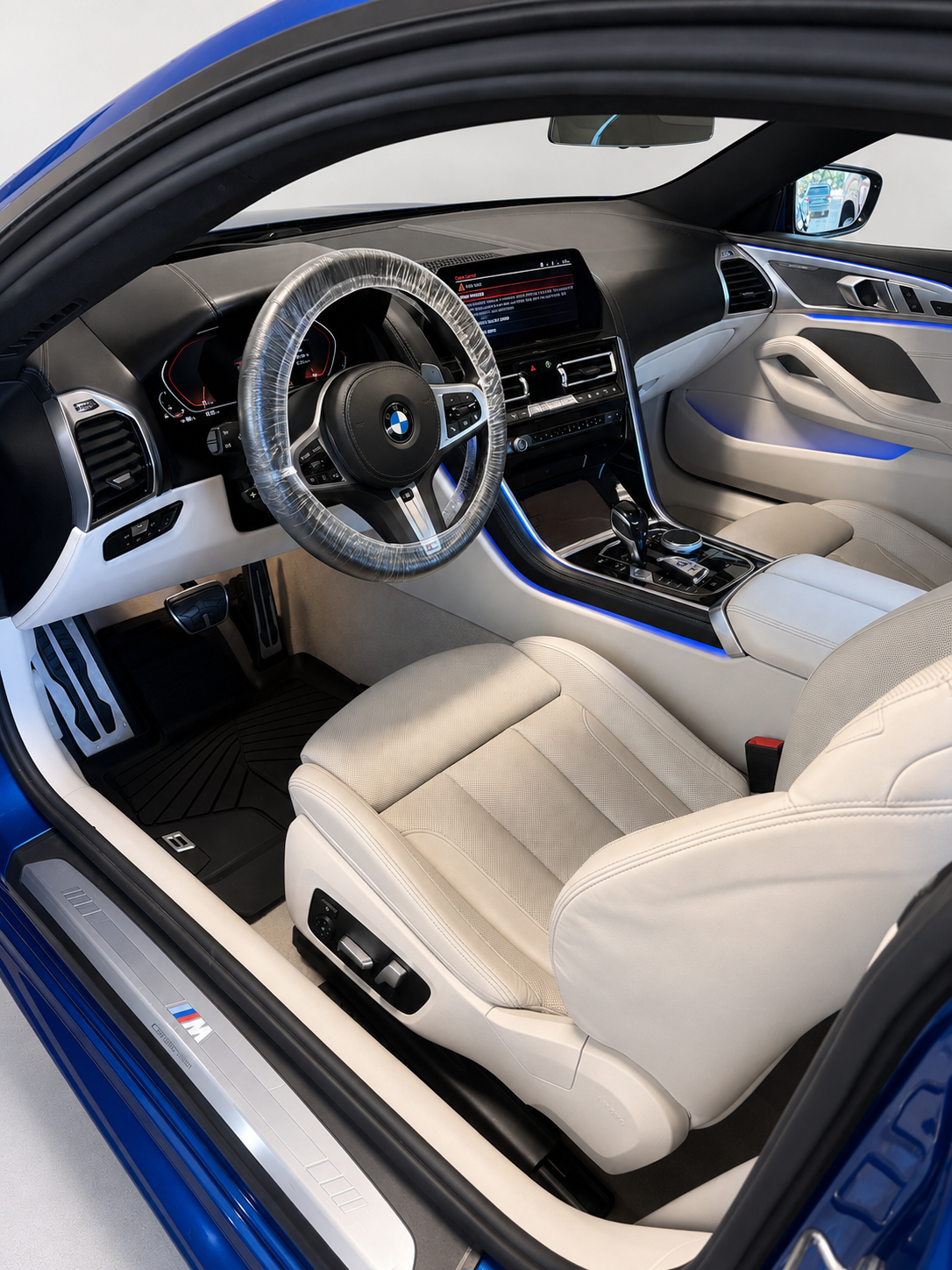 Interior of a blue BMW car showing the driver's seat, steering wheel, dashboard, and center console with gear shift and control buttons.